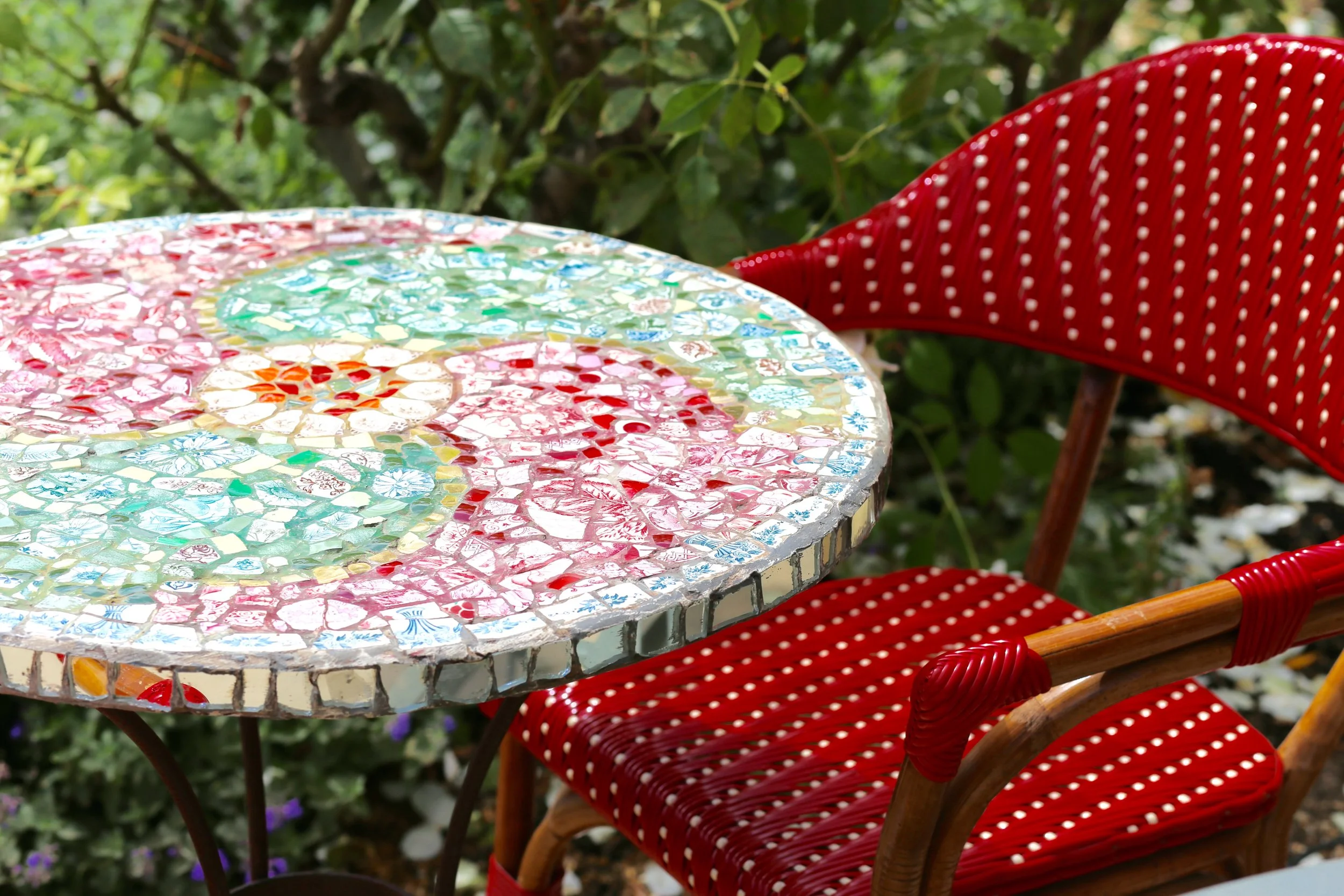 Colorful mosaic tabletop with a red polka dot chair and green leafy background.