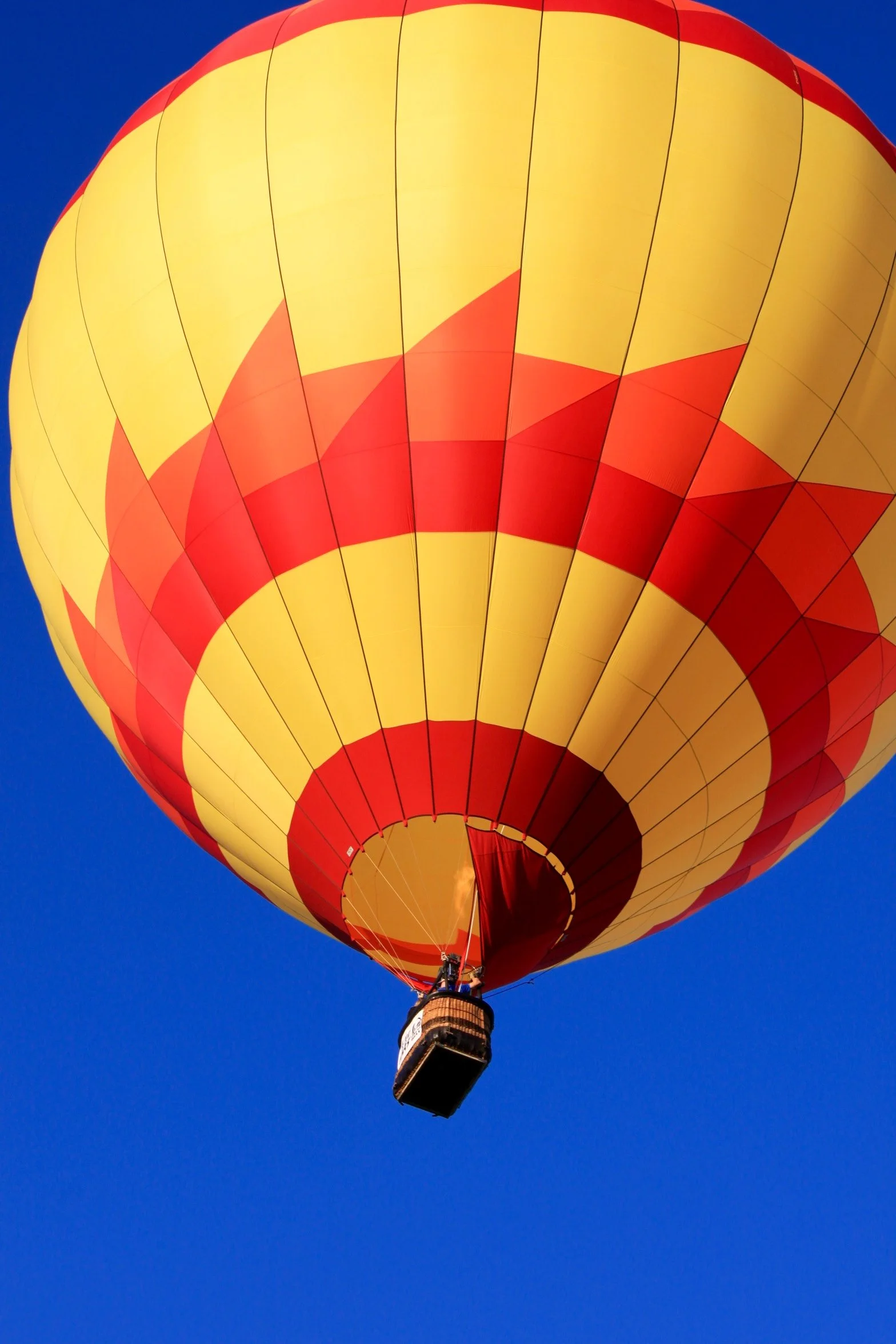 A hot air balloon with yellow and red checkered pattern floating in a clear blue sky flying over Napa CA