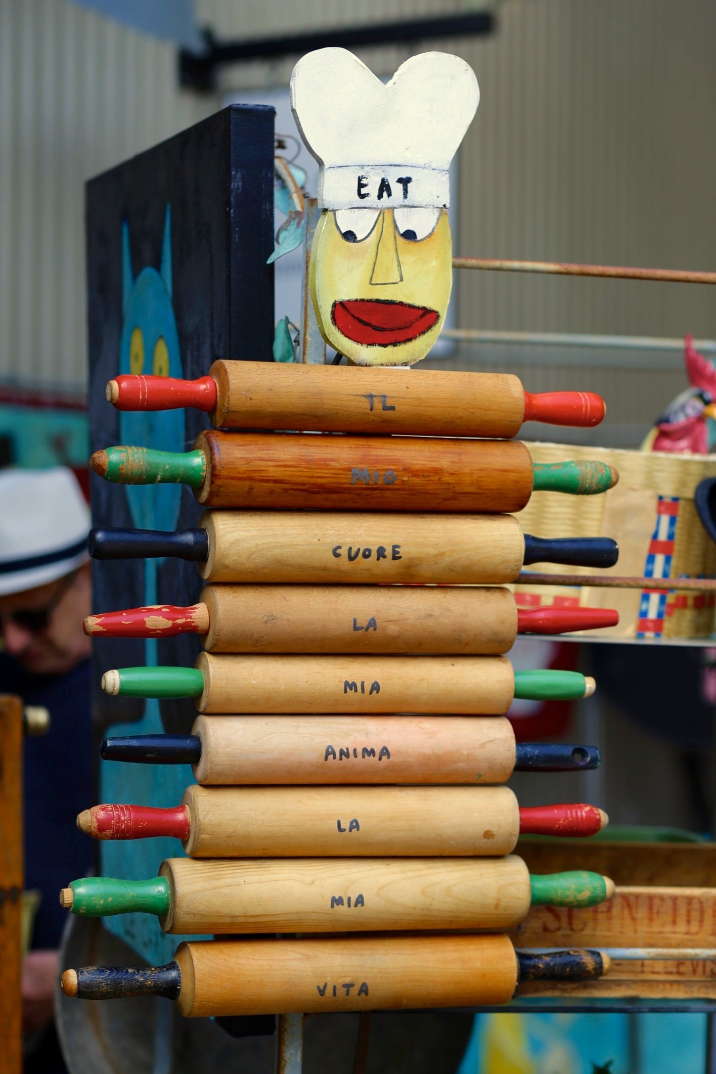 A colorful xylophone with wooden bars and painted tips, labeled with Italian names of musical notes, stacked vertically. A puppet face wearing a chef's hat with the word 'EAT' made of rolling pins, to market the culinary institute in Napa