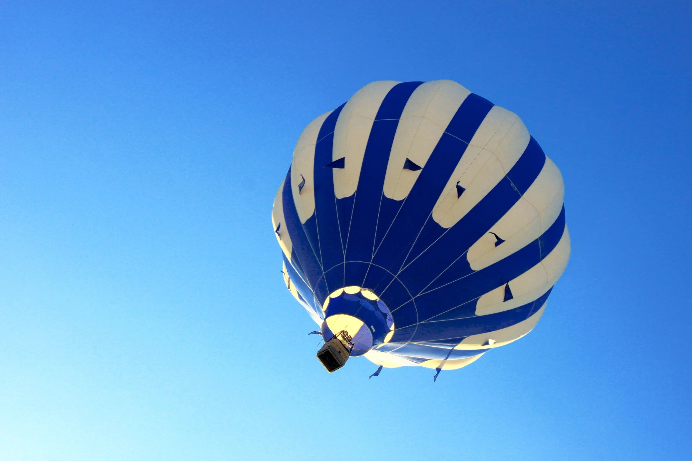 A hot air balloon with a white and navy blue striped pattern flying in a clear blue sky flying over the Napa Valley.
