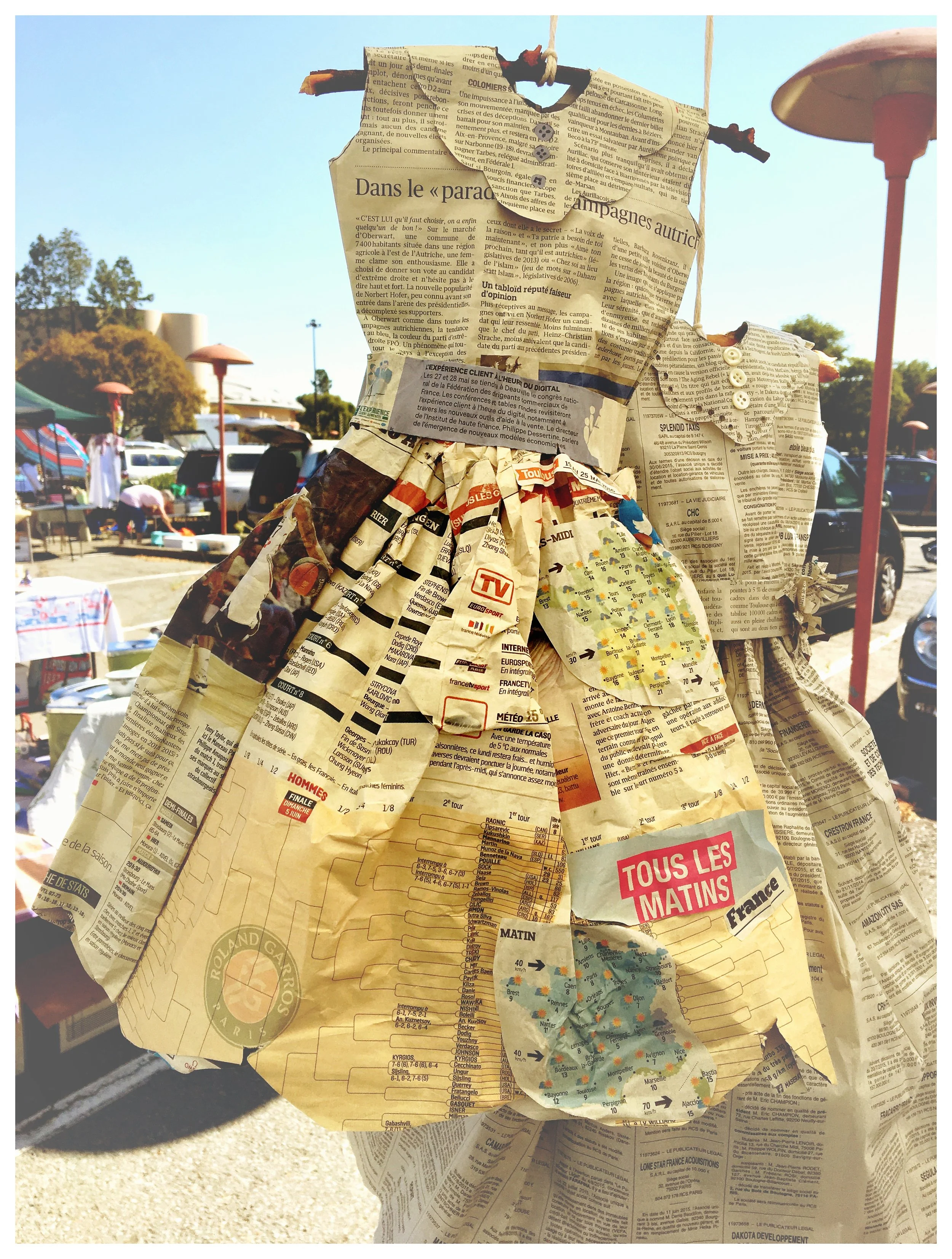 A sculpture made of crumpled and layered newspapers attached to a stick with two white buttons, made out of French Newspaper. Sold at a vintage fair in Napa Valley