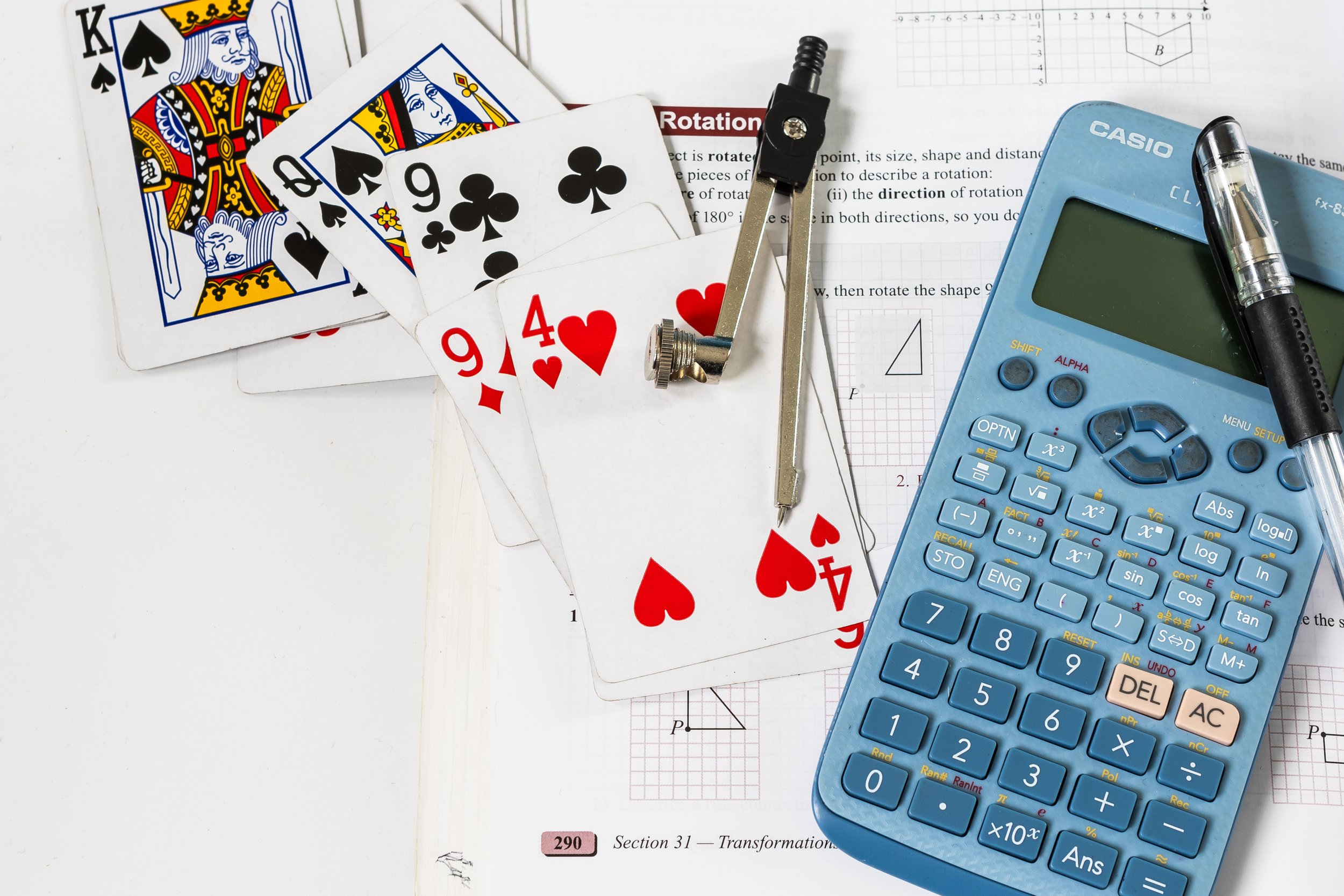 Maths learning materials — playing cards, geometry compass, scientific calculator, and KS3 transformations textbook
