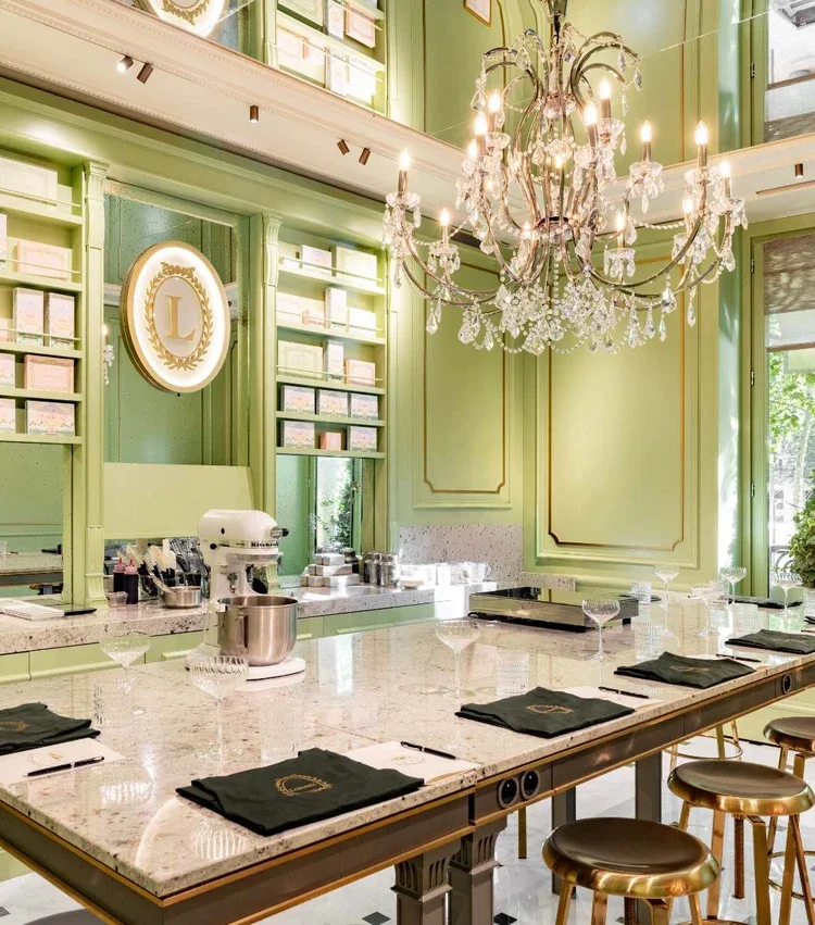 Elegant dining room with a large marble table, black napkins, crystal glasses, a chandelier, and green walls with built-in shelves and a window in the corner.