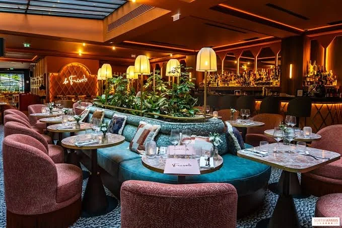 Uptown restaurant interior with pink upholstered chairs, marble tables, a curved blue sofa, and warm ambient lighting.