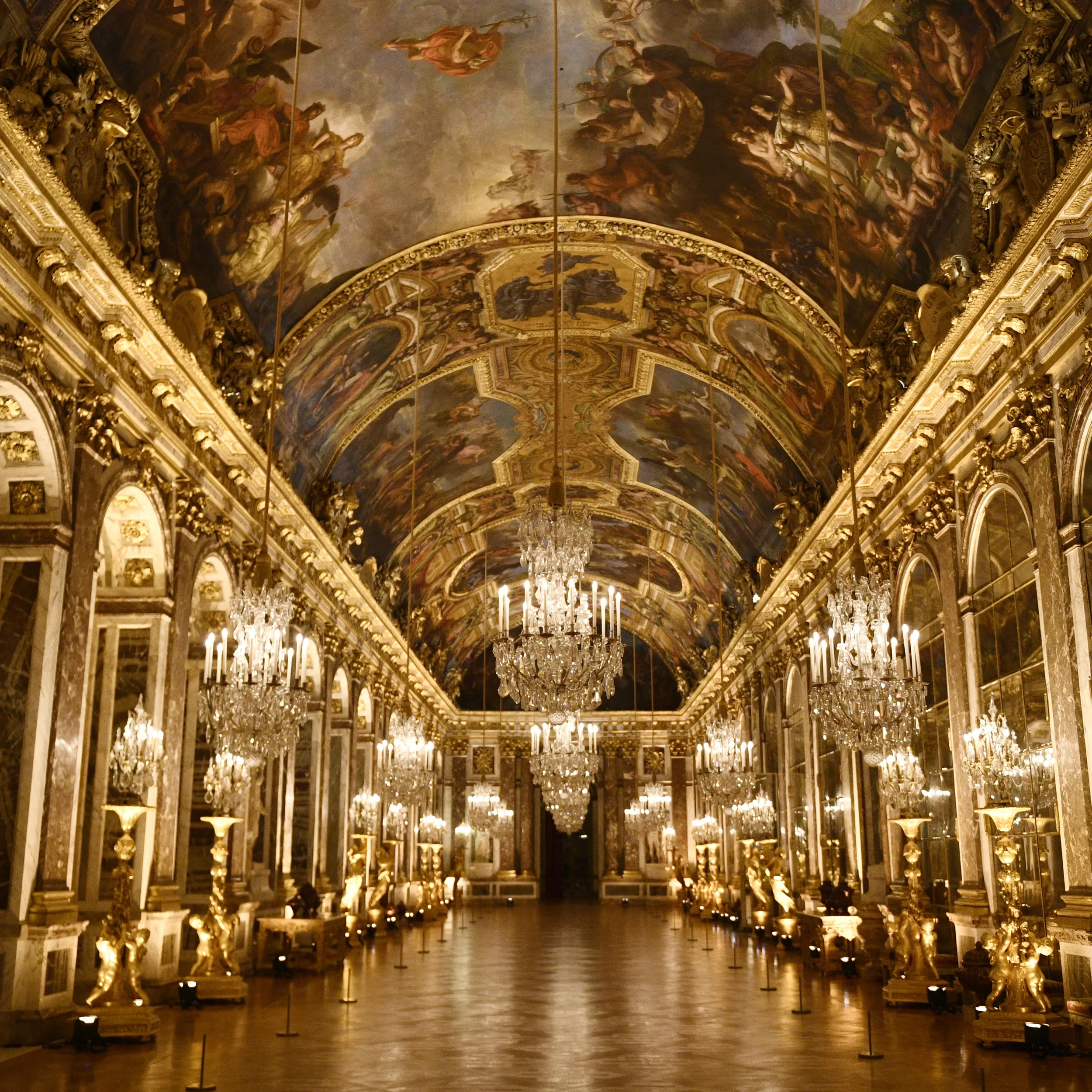 Opulent gold and white hall filled with chandeliers, ornate gilded sculptures, and elaborate ceiling frescoes depicting mythological scenes.