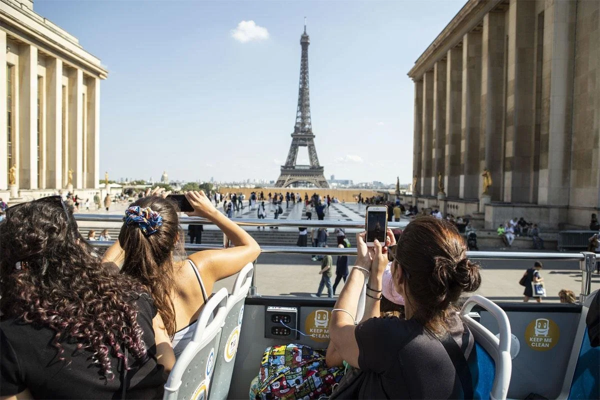 Three women on a double-decker bus taking photos of the Eiffel Tower in Paris.