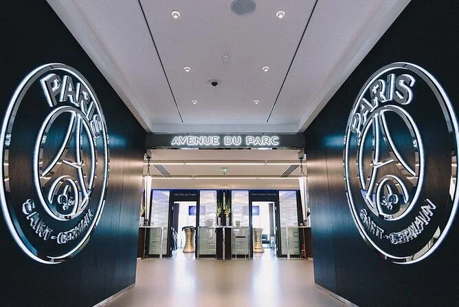 Entrance hallway of Paris Saint-Germain football stadium with illuminated PSG logos on black walls and a sign reading 'Avenue du Parc'