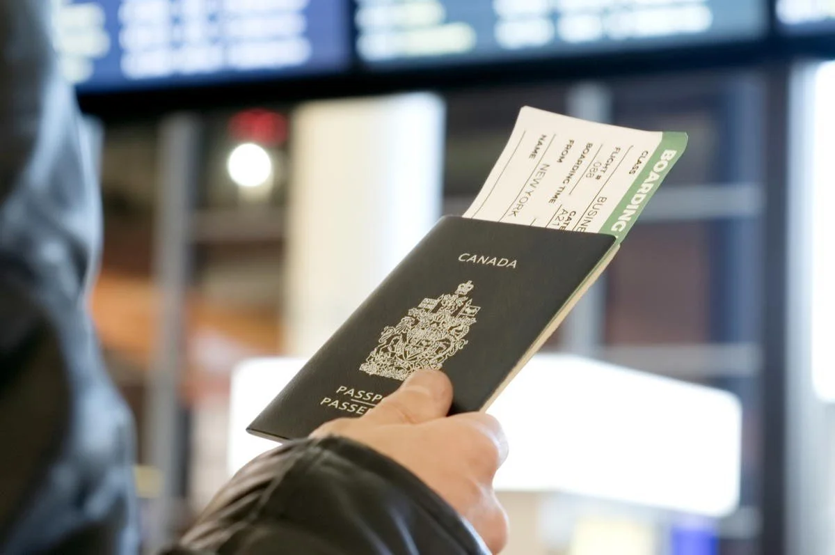 Person holding a Canadian passport with a boarding pass tucked inside at an airport.