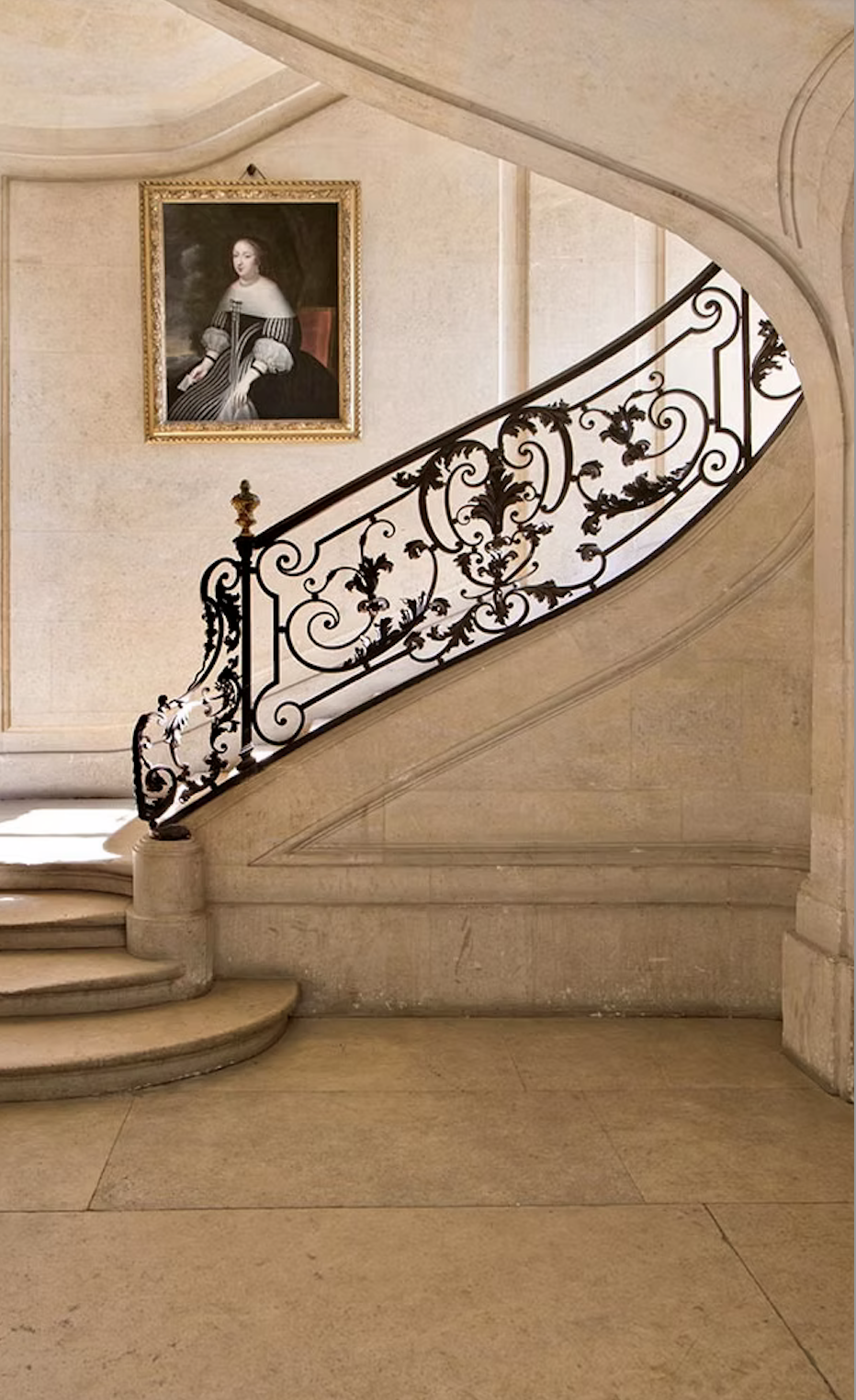 Elegant interior staircase with ornate black wrought iron railing, beige stone walls, and a portrait of a woman in historical attire hanging on the wall.
