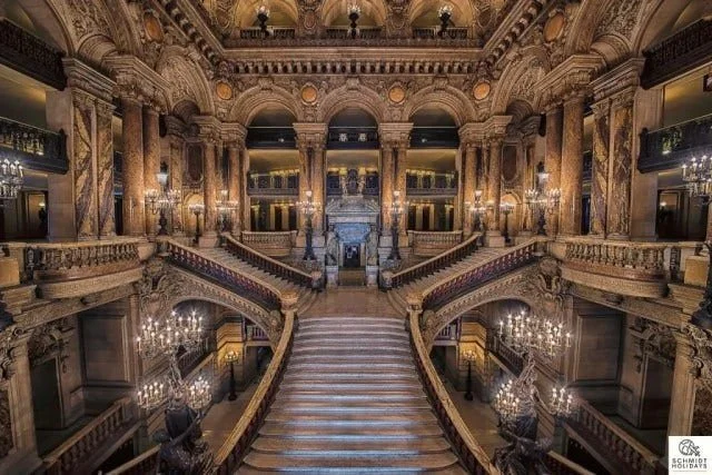 Luxurious historic hotel lobby with grand staircase, ornate arches, and chandeliers.