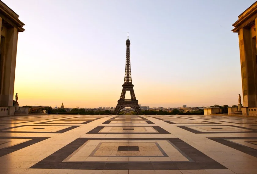 Eiffel Tower in Paris seen from Trocadéro at sunset with patterned ground in the foreground and statues framing the scene.