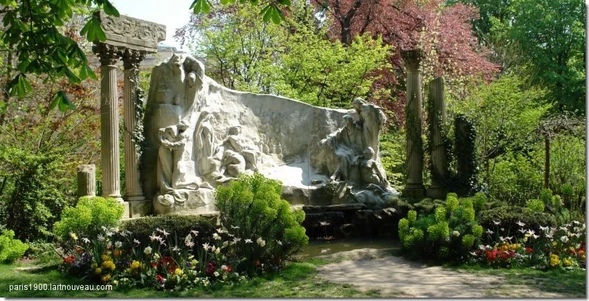 A marble sculpture of allegorical figures surrounded by lush greenery and colorful flowers in a garden.