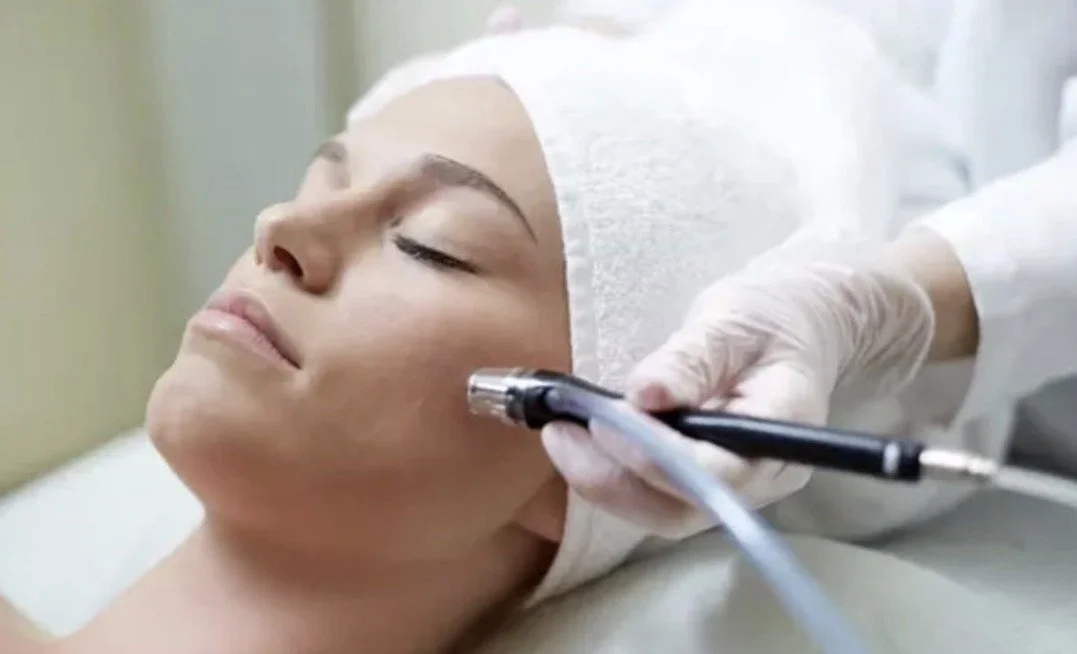 A woman lying down with her eyes closed as a medical professional uses a pen-like device for a facial treatment.