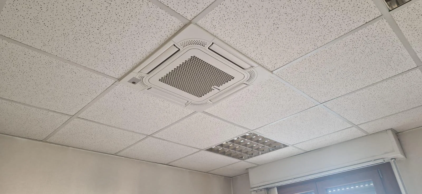 Soffitto d'ufficio con pannelli acustici, ventola di condizionamento e una luce a pannello.
