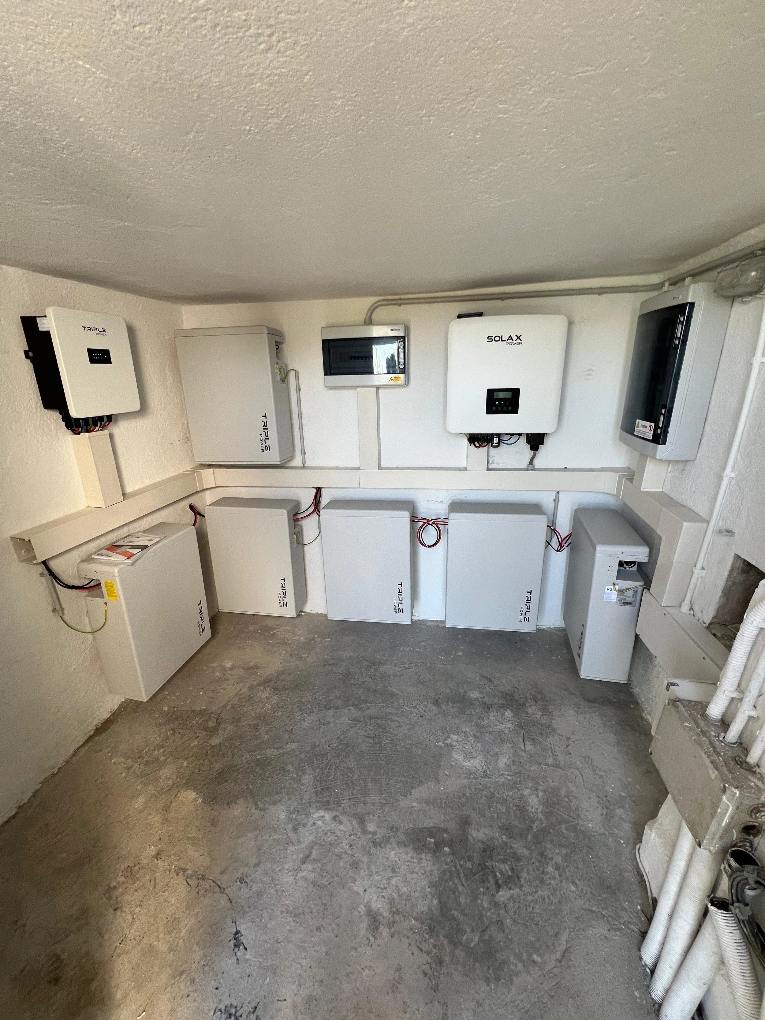 Pannelli solari e inverter installati su una parete di una stanza di un edificio, con alcuni pannelli e cablaggi visibili.