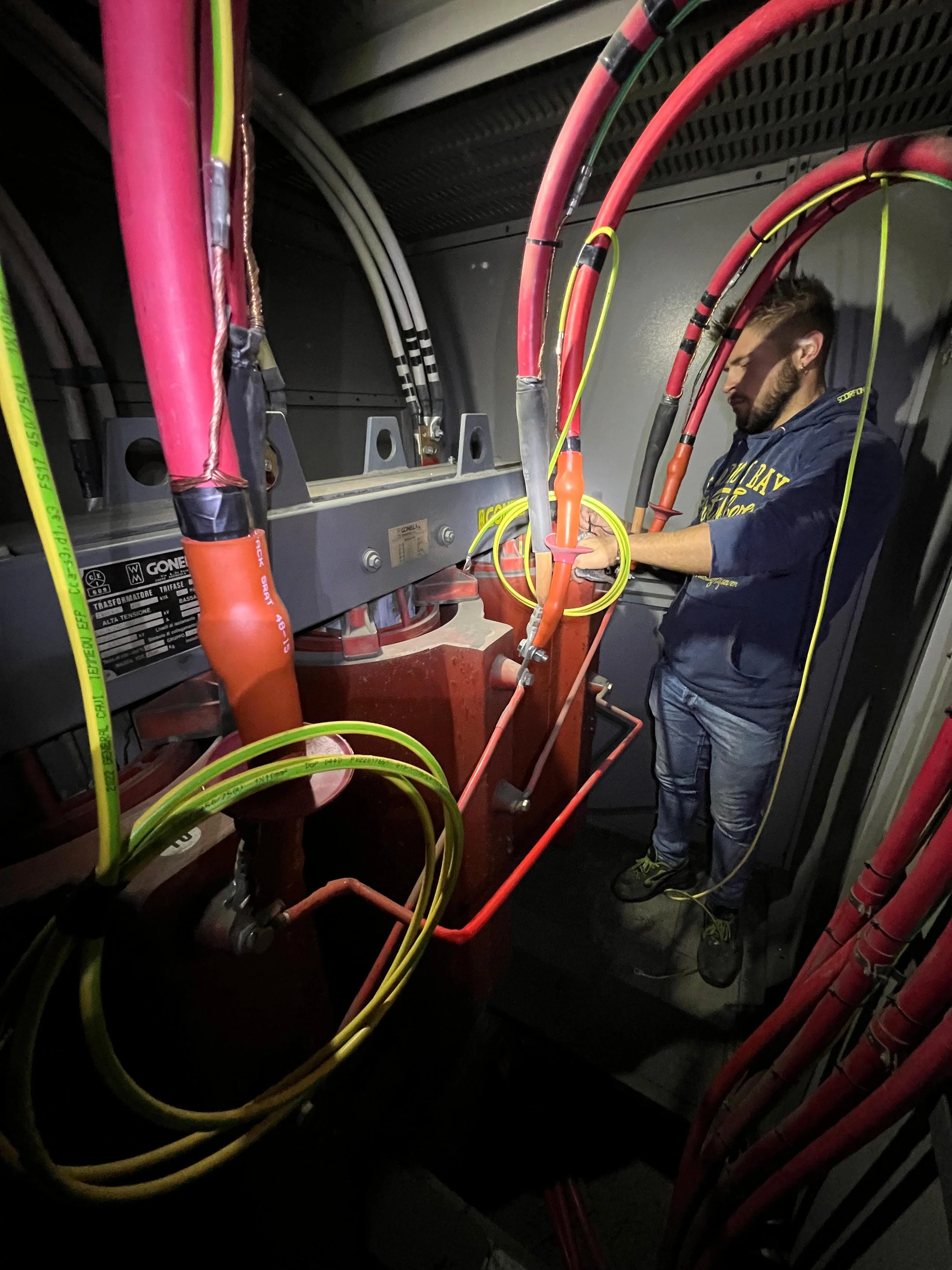 Un uomo che lavora su un pannello di controllo elettrico con cavi colorati di rosso, giallo e nero, nel contesto di un'apparato industriale o di cablaggio.