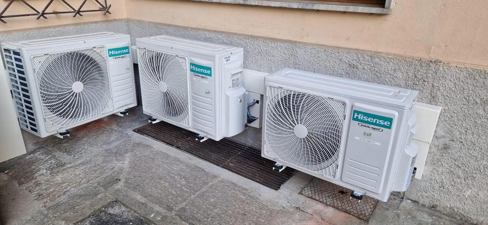 Tre unità di aria condizionata Hisense installate all'esterno di un edificio, affacciate su un marciapiede di pietra.