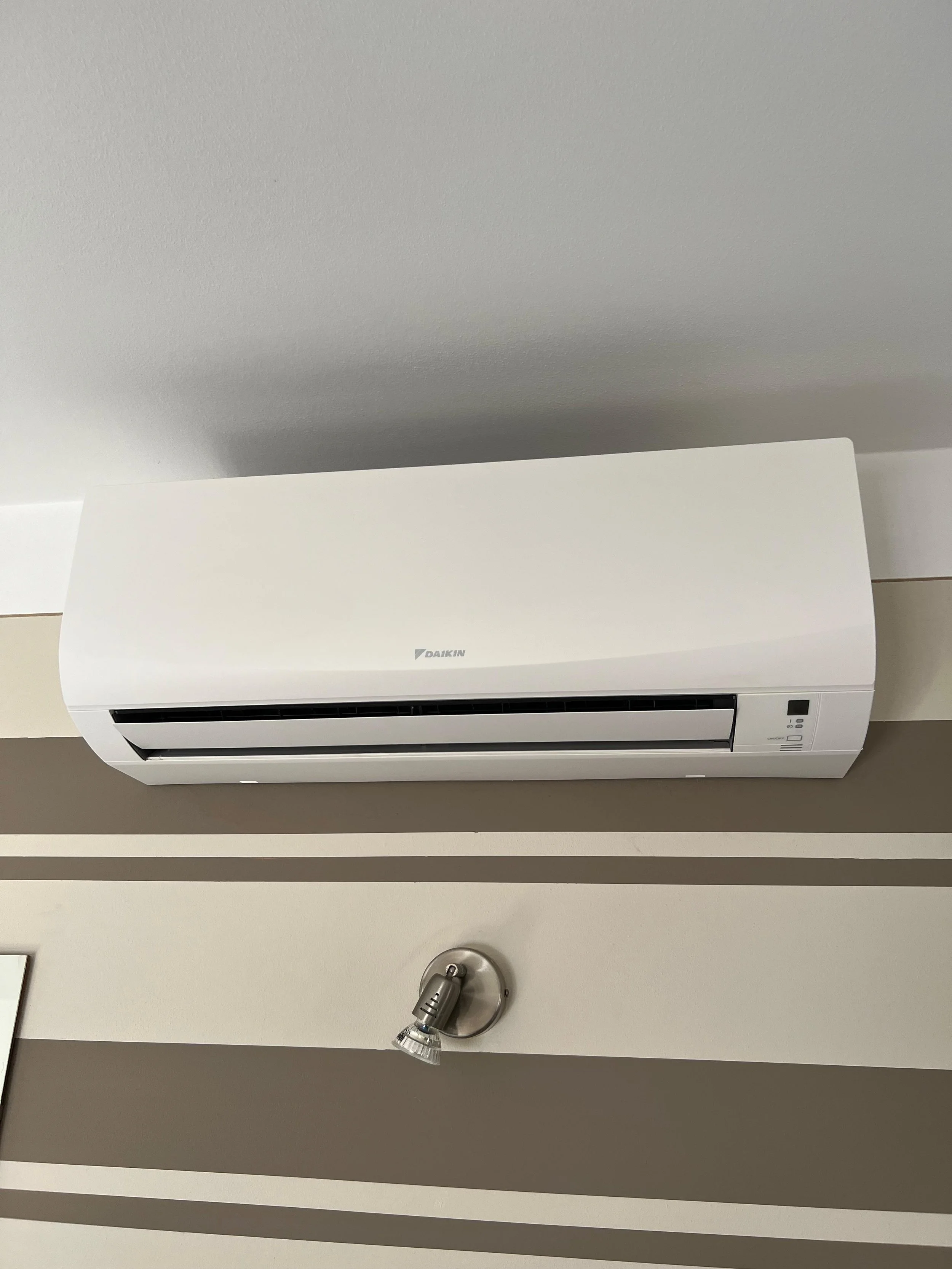 Climatizzatore Daikin installato sulla parete di una stanza, con una lampada regolabile sotto di esso, illuminando la parete.