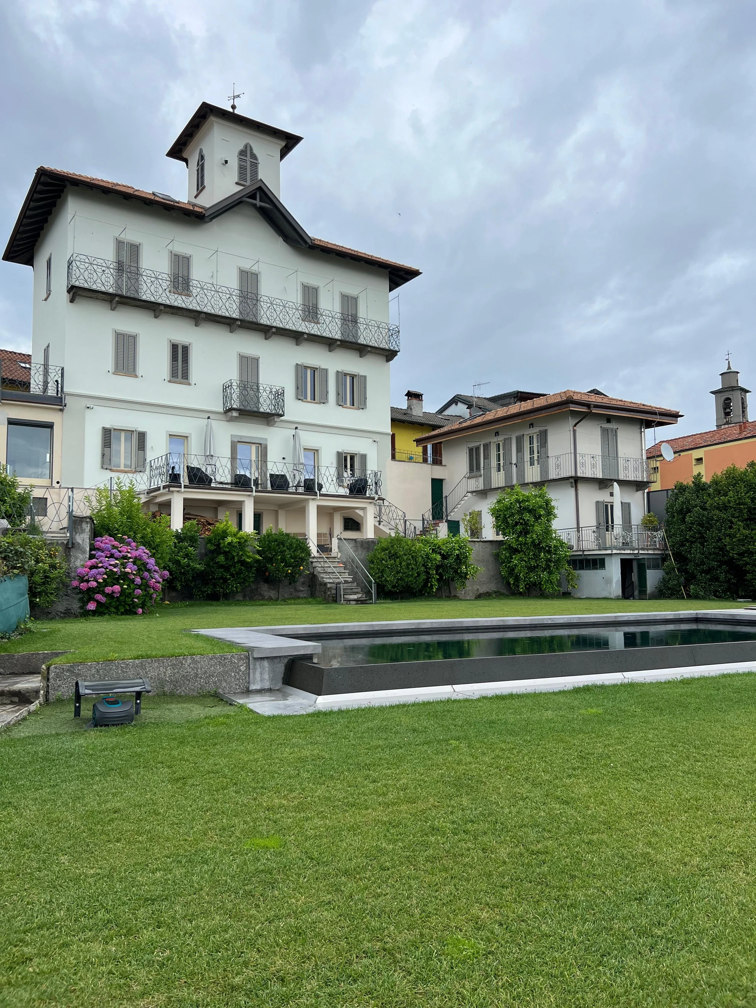 Giardino con prato verde, piscine e case residenziali sullo sfondo.