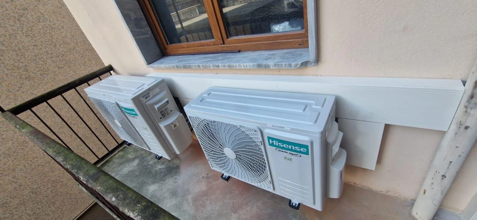 Due unità esterne di aria condizionata di marca Hisense installate su un balcone con finestra in legno.