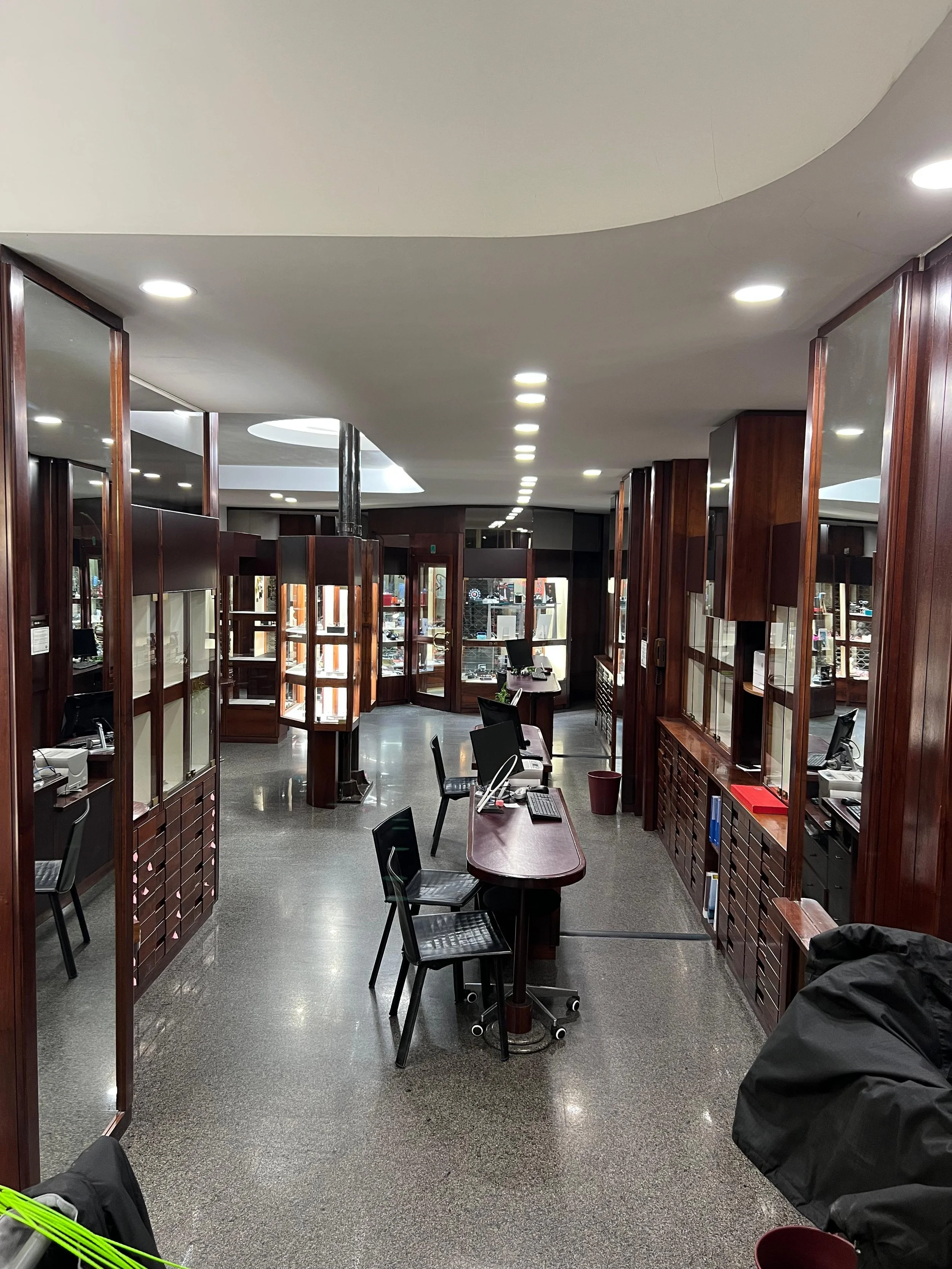 Interno di un negozio con scaffali di legno, attrezzature di computer e sedie, illuminazione a soffitto