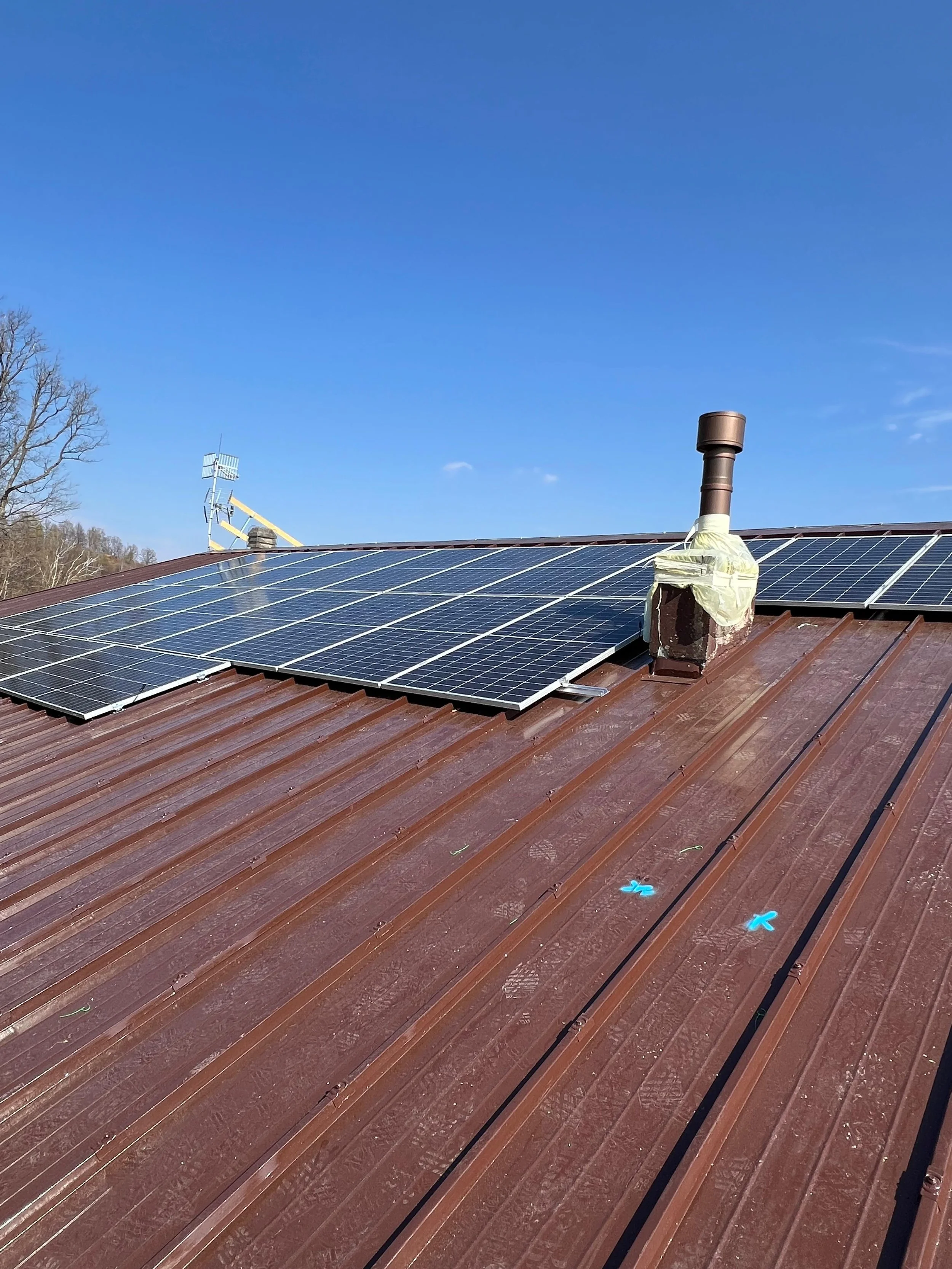 Tetto di una casa con pannelli solari installati, camino e alcune apparecchiature sul tetto, sotto un cielo blu.