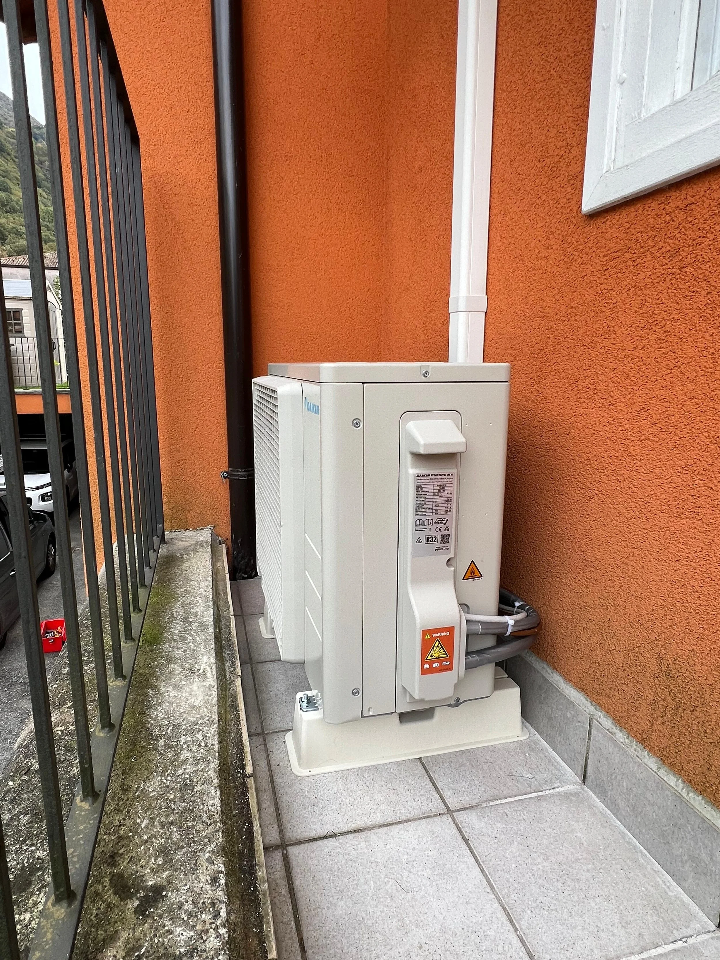 Un'unità di trattamento dell'aria installata all'esterno di un edificio, con pareti arancioni e una finestra bianca, posizionata sulla parete di un edificio.
