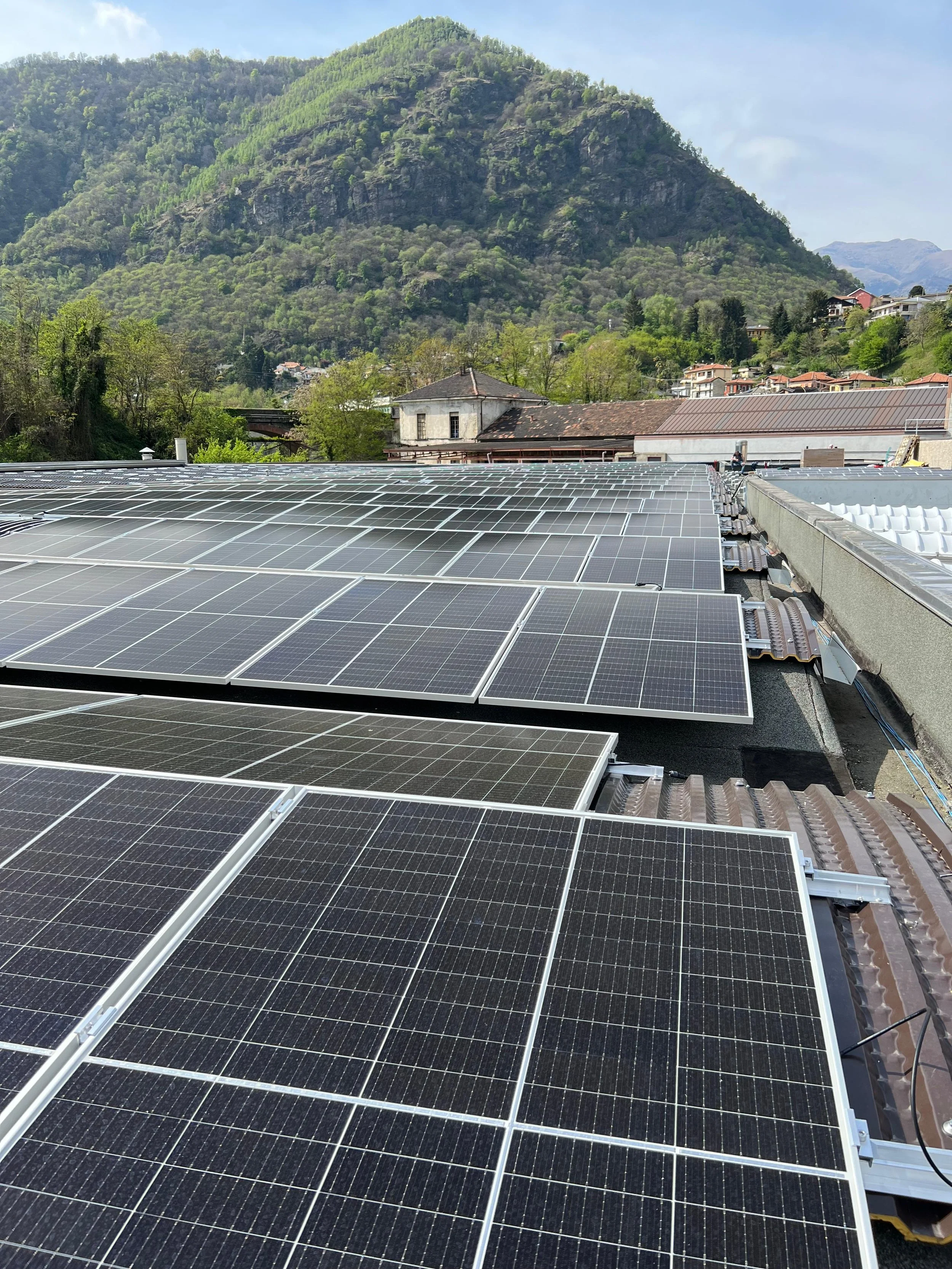 Pannelli solari installati sul tetto di un edificio con un paesaggio montuoso e case sparse sullo sfondo.