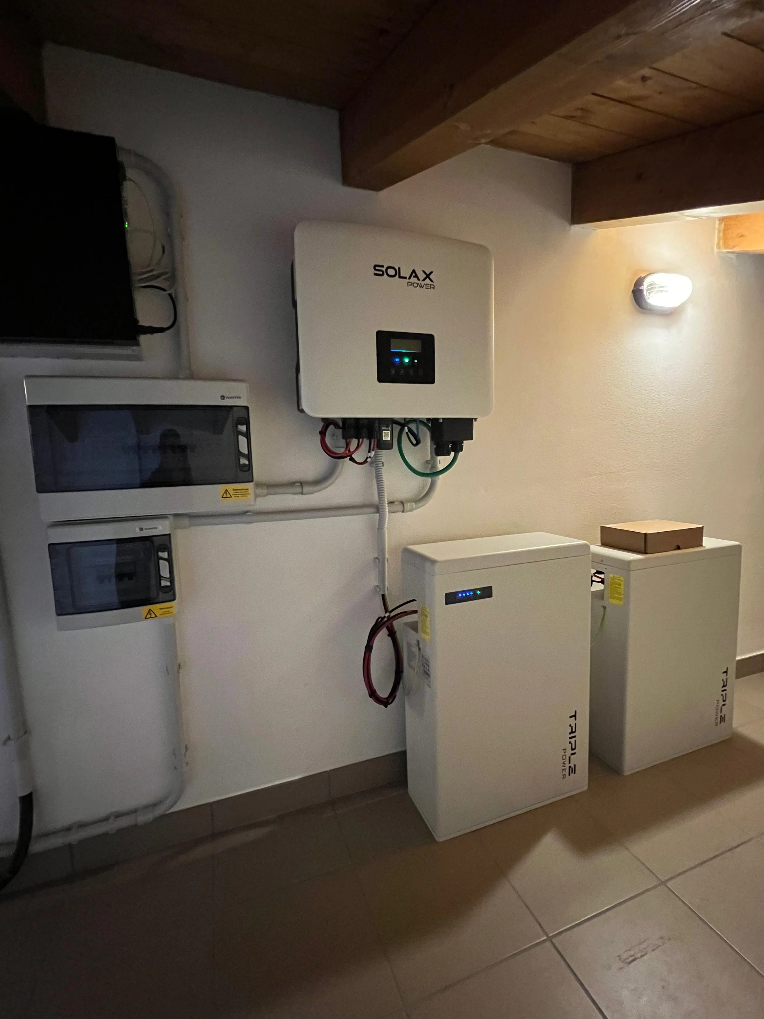 Installazione di un sistema di pannelli solari. Sono visibili vari dispositivi e collegamenti elettrici sulla parete, inclusa una scatola di distribuzione, un inverter Solax Power e altri componenti elettrici, su una parete bianca.
