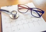 A calendar, a stethoscope, and a pair of glasses on a desk.