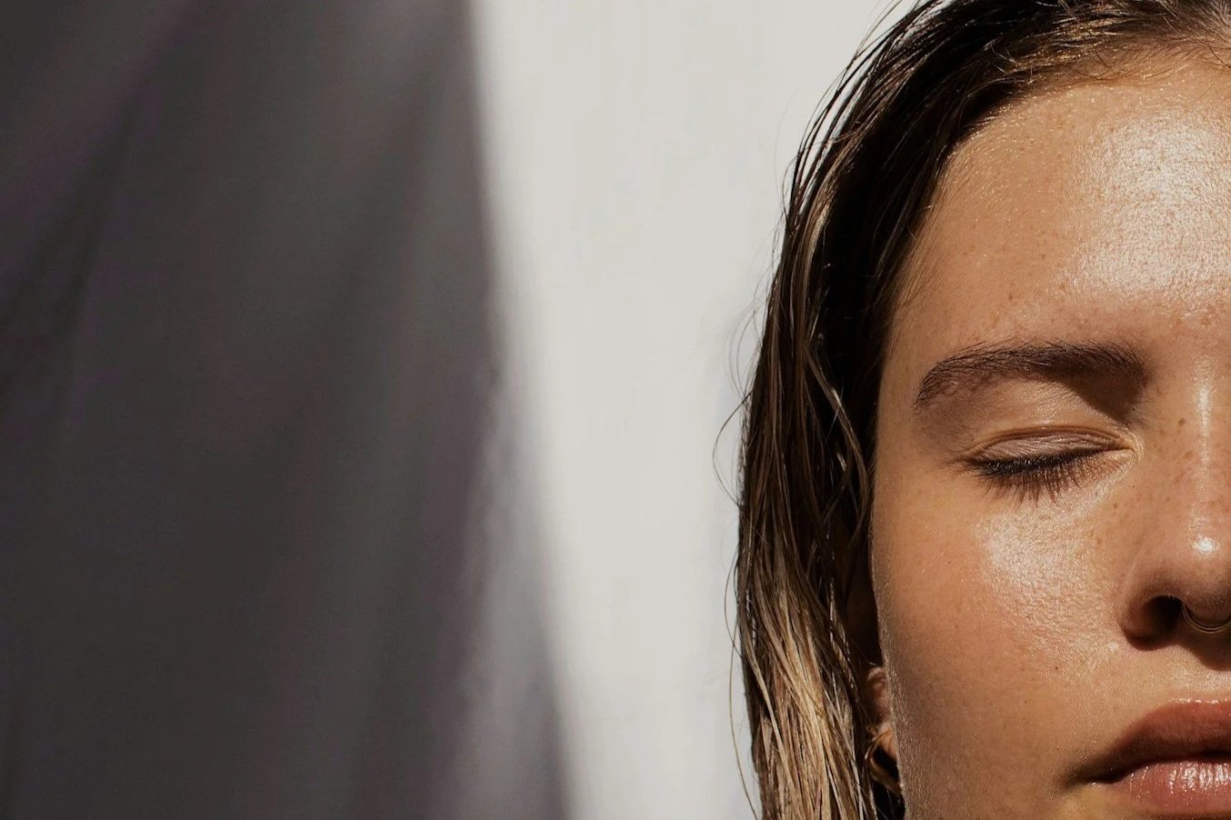 Close-up of a young woman with her eyes closed, showing her face with natural makeup and wet hair, against a neutral background.