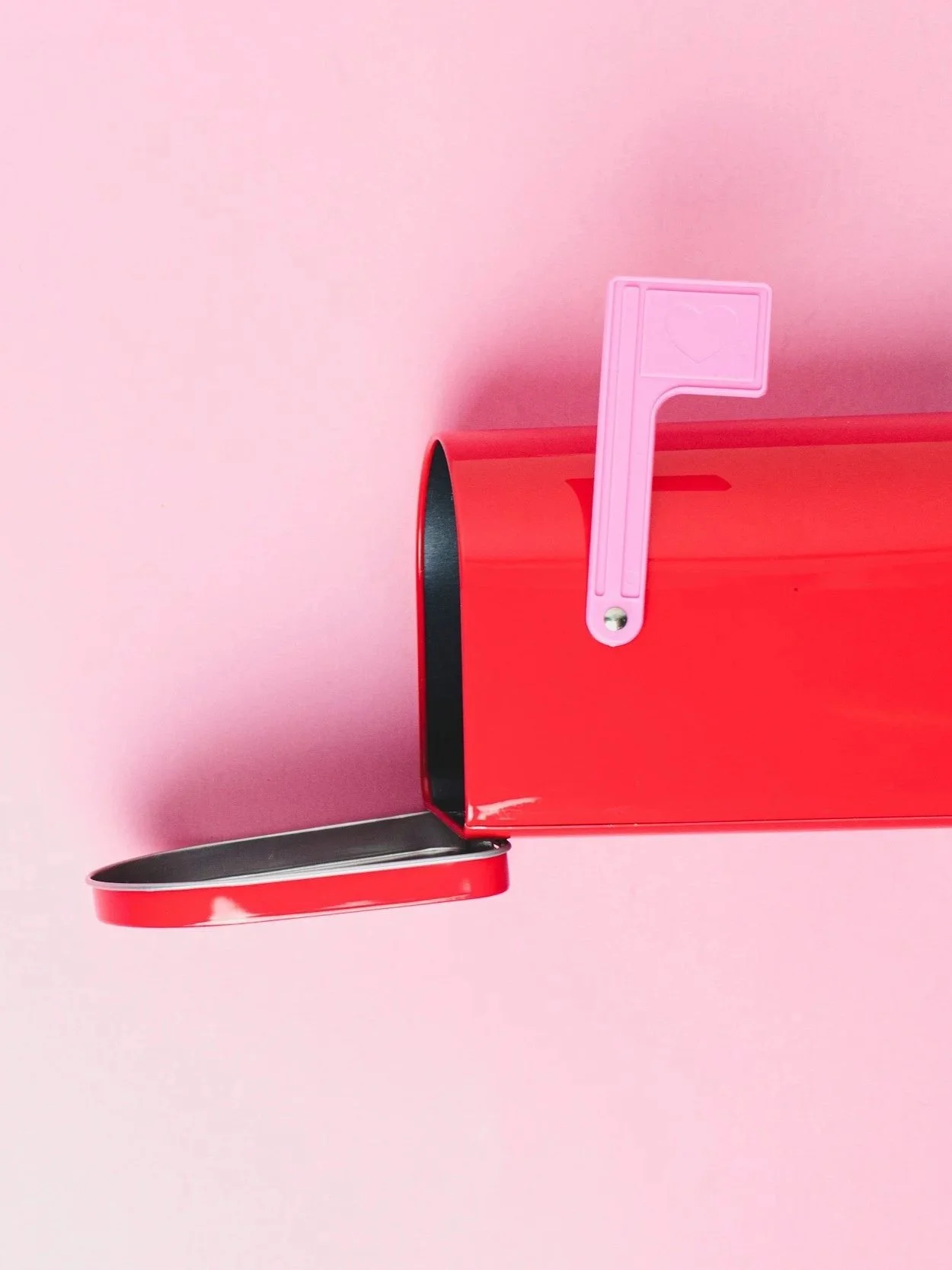 A red mailbox with its door open on a pink background, with a pink flag featuring a heart symbol attached to the side.