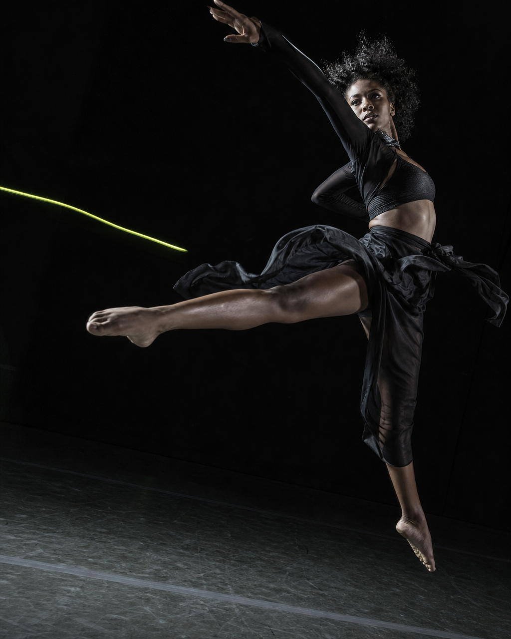 Contemporary dancer leaping in a black studio with electric lime light