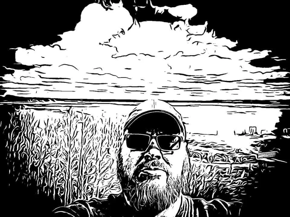A black and white stylized digital illustration of a man with a beard, wearing sunglasses, a cap, and a jacket, taking a selfie outdoors. The background includes a vast sky with clouds, a field of tall crops, and a distant landscape with buildings.