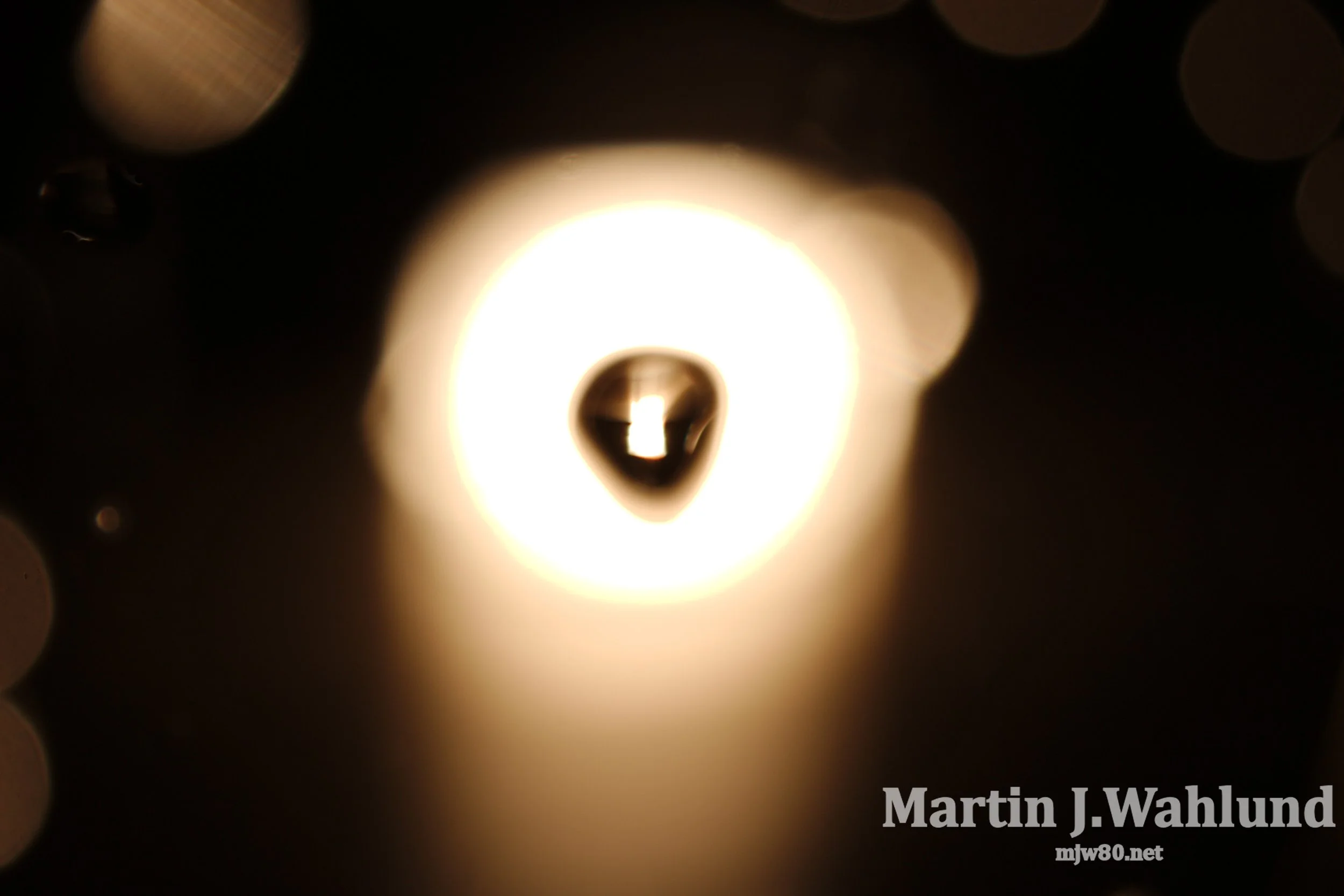 Close-up of a lit light bulb with a bright glow surrounded by darkness, with the text "Martin J. Wahlund" and "mtw80.net" at the bottom right corner.