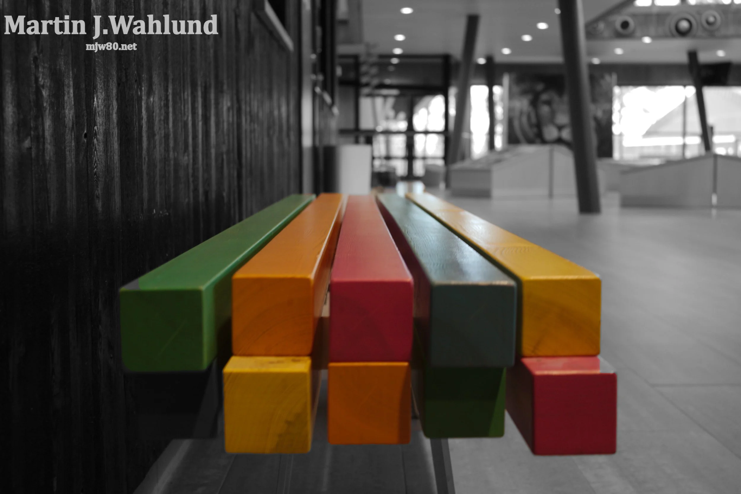 Colorful wooden blocks arranged in a row along a dark wall in a public indoor space with modern architecture and bright lighting.