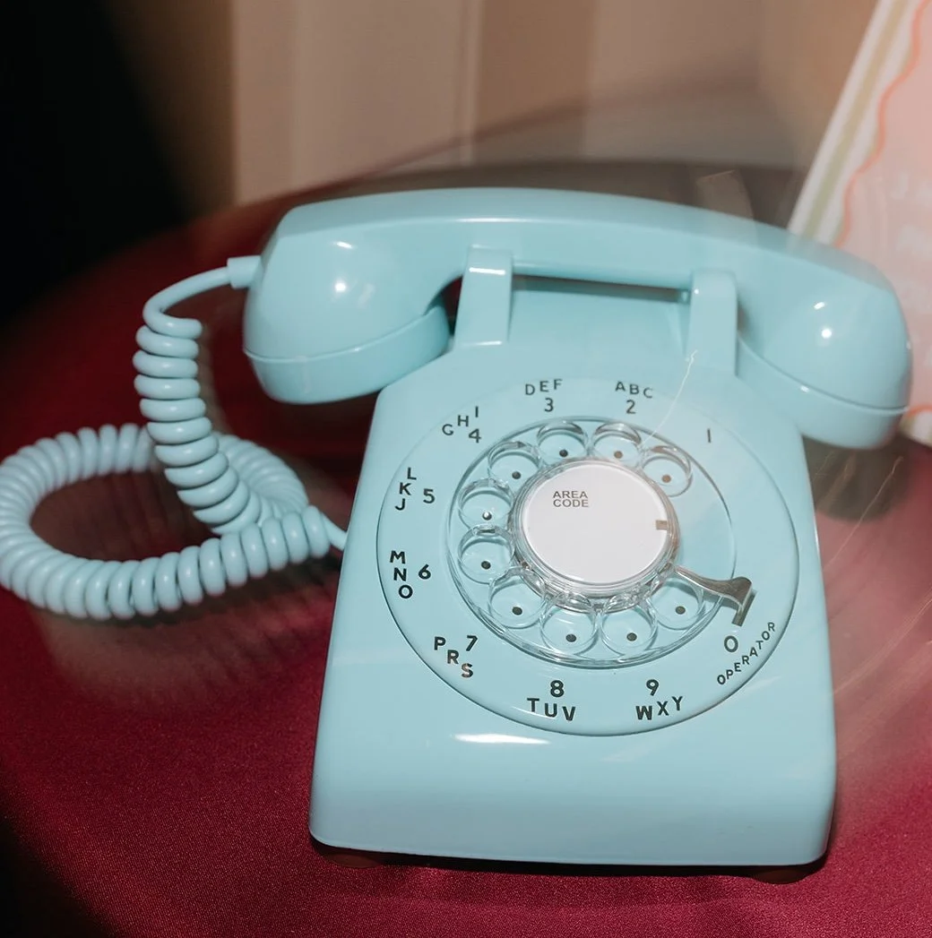 A light blue rotary telephone on a red surface, with a clear plastic cover on the dial area.