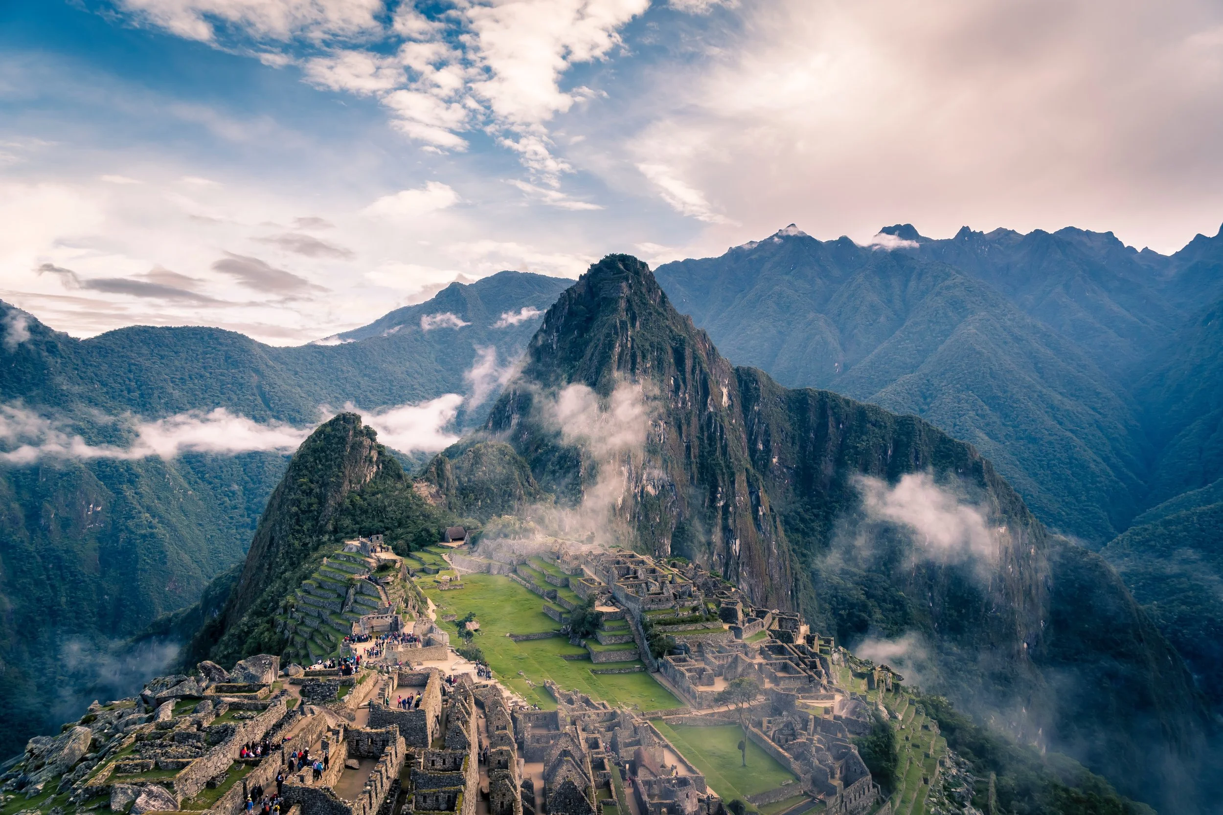 Ancient Incan ruins at Machu Picchu with mountain peaks in the background, lush greenery, and scattered clouds.