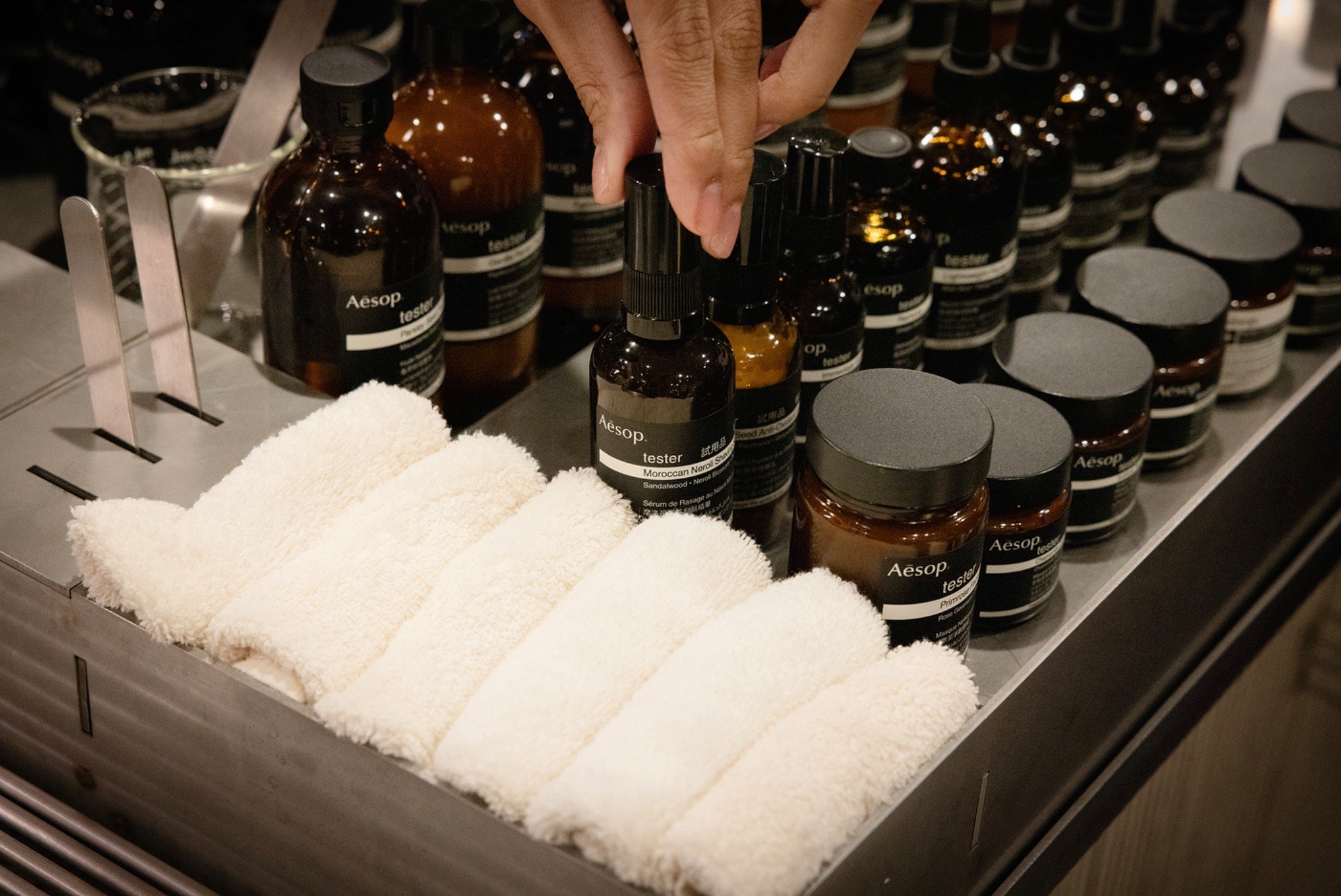 A guest selecting an Aesop product tester beside neatly rolled white towels.