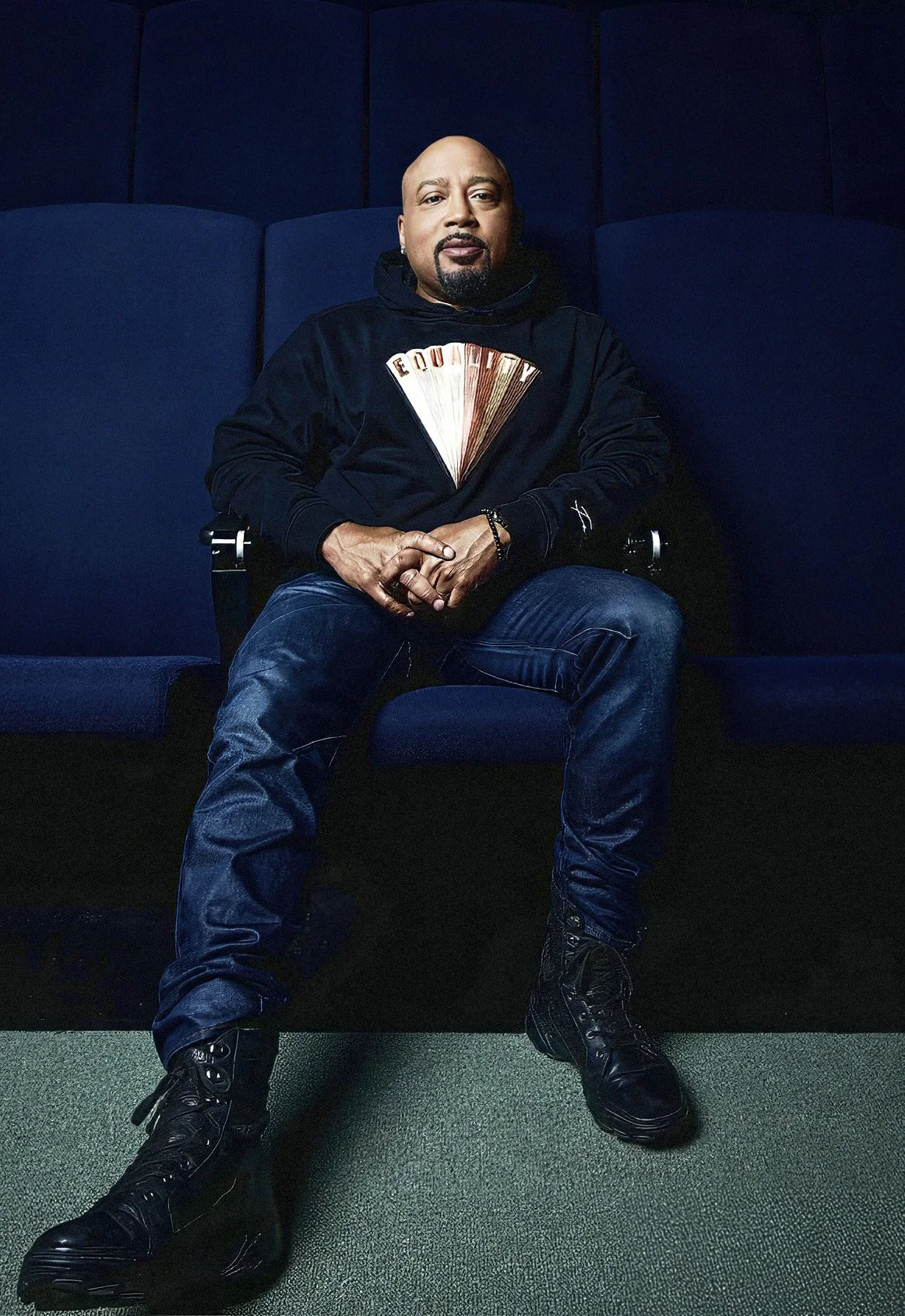 Portrait of entrepreneur Daymond John seated among dark blue theater seats.