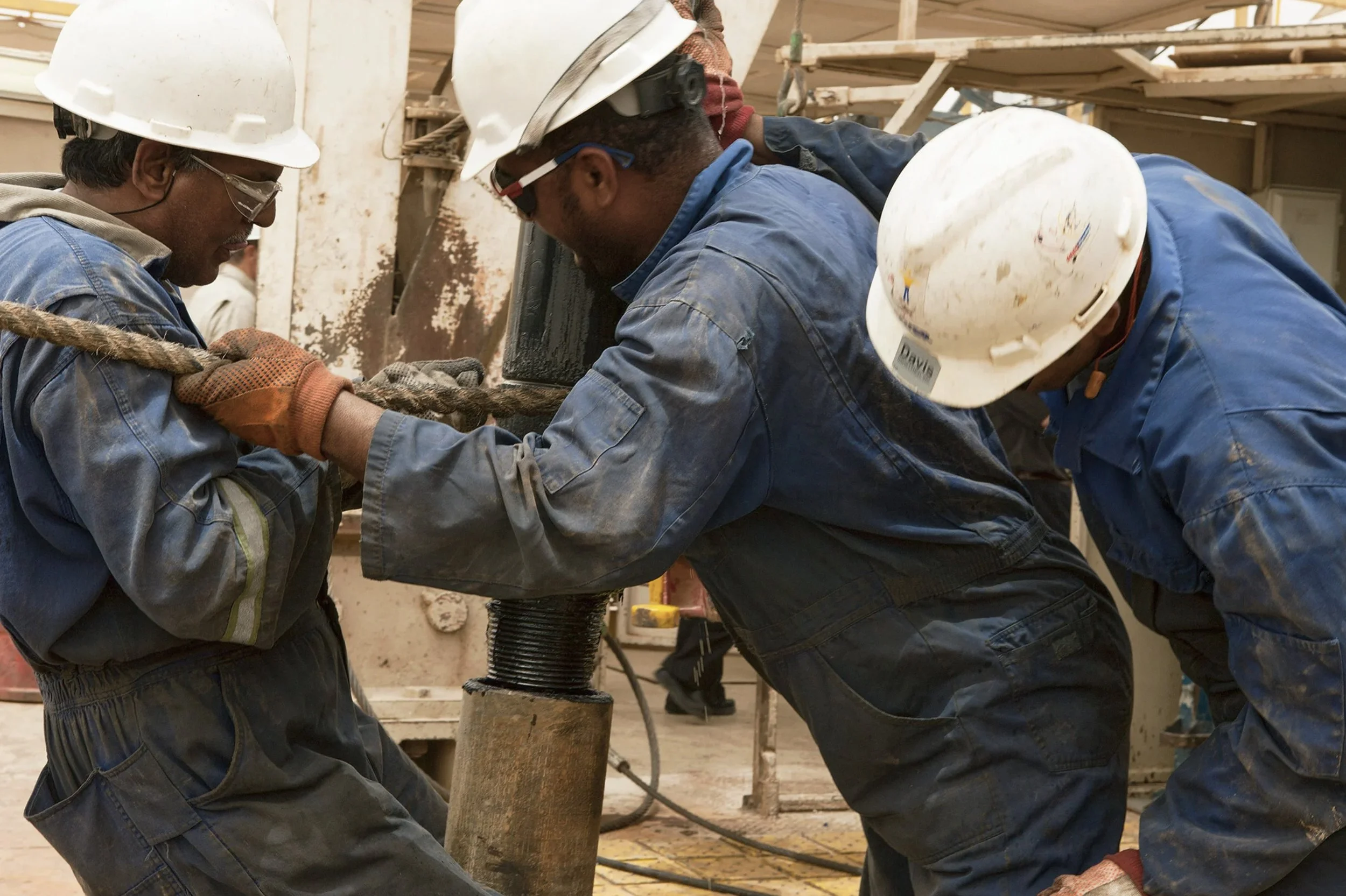 Industrial workers in hard hats collaborating on equipment at a Chevron facility.