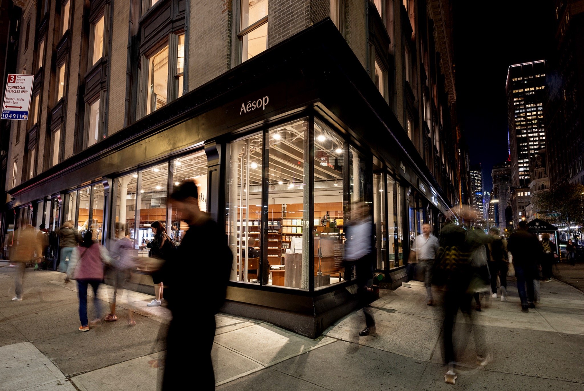 Aesop’s illuminated NoMad storefront at night, with pedestrians moving along the New York sidewalk.
