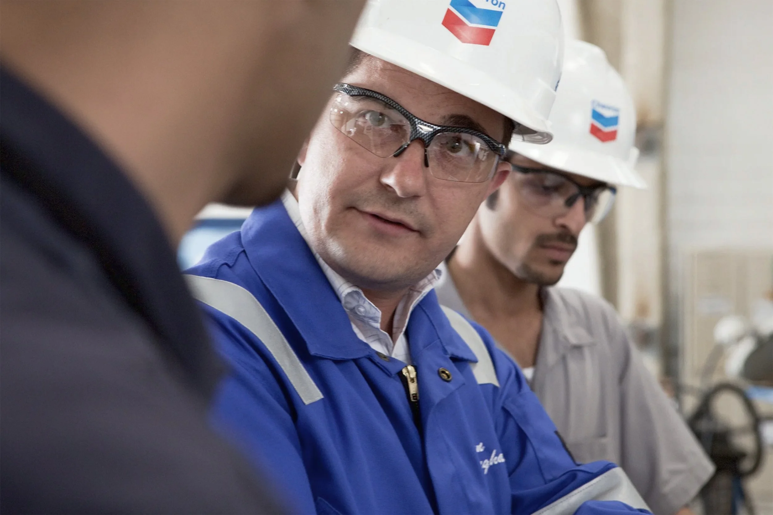 Chevron employees wearing hard hats and safety glasses working inside an industrial facility.