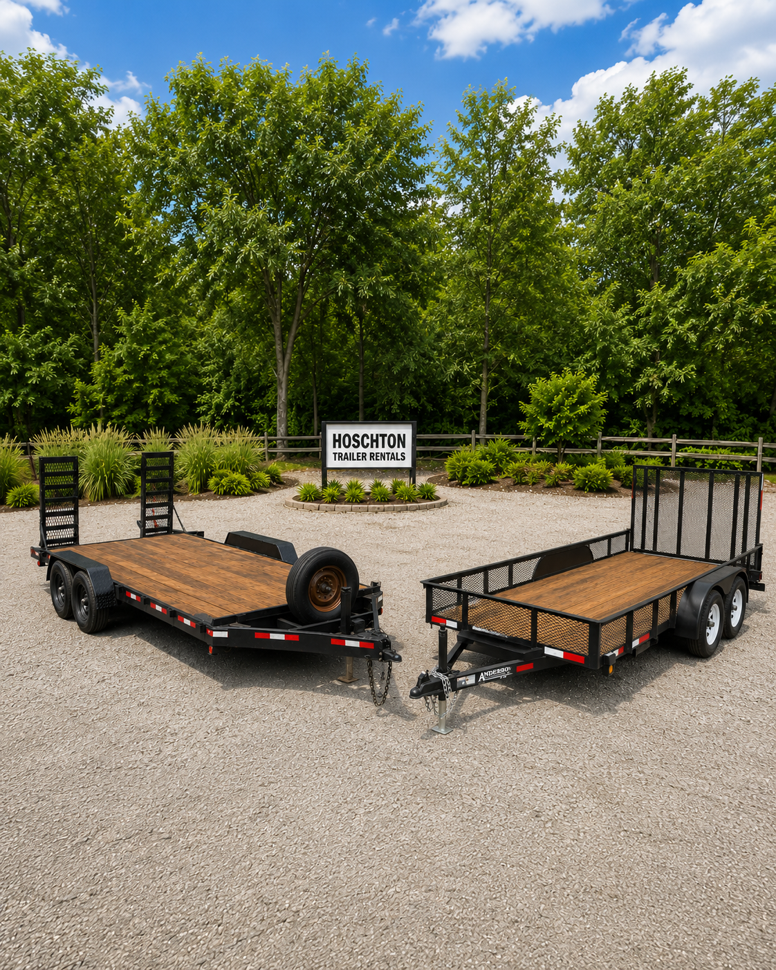 Two flatbed trailers with wood decks parked on gravel ground in front of trees and a sign that says 'Hoschton Trailer Rentals'.