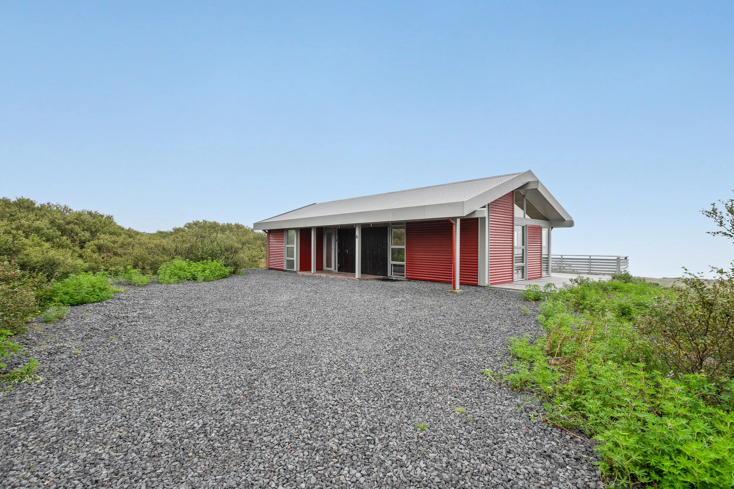 A red house with a white roof surrounded by greenery on a gravel driveway.