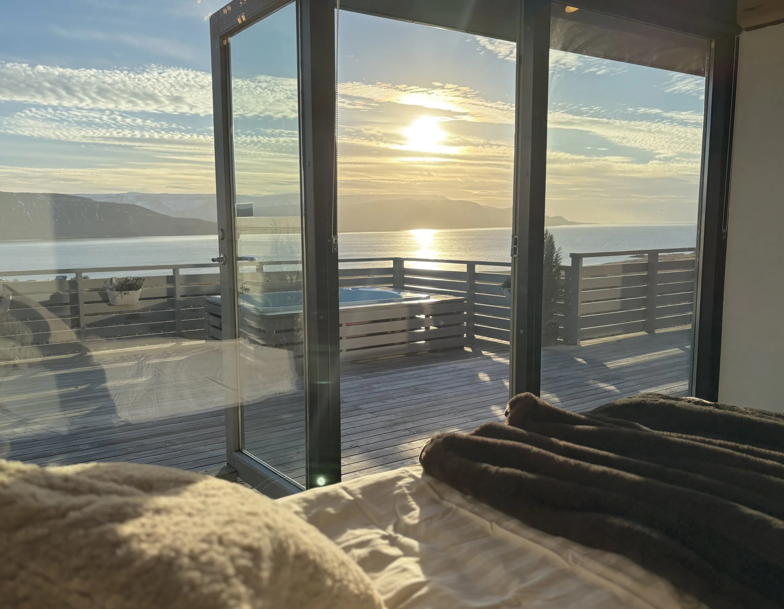 Sunset view through glass doors onto a deck with a hot tub and a mountain lake in the background.
