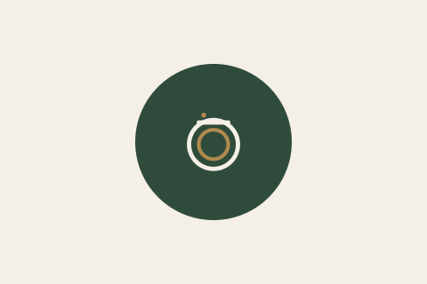 A camera icon inside a dark green circle on a beige background.