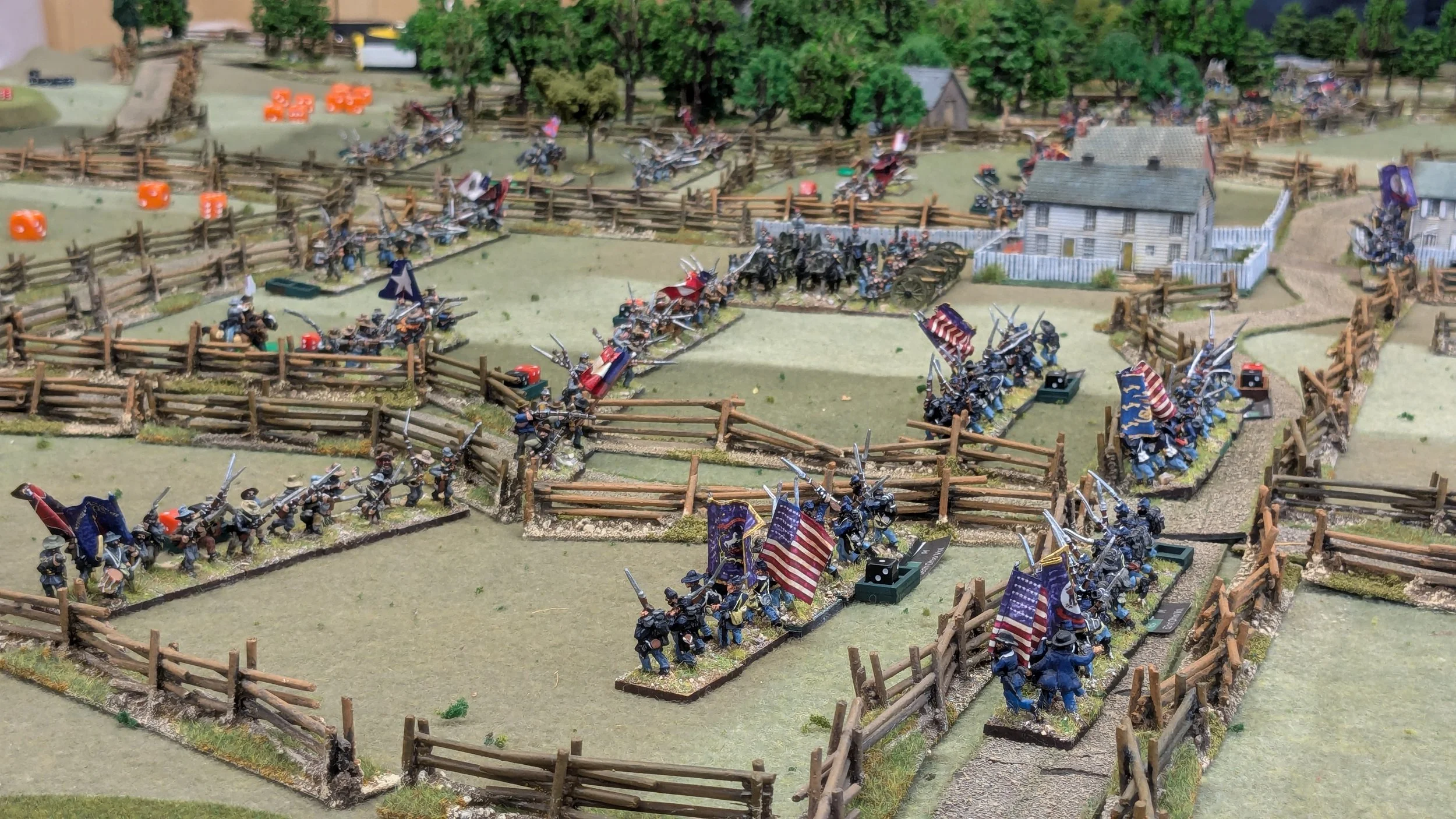 Miniature diorama of a Civil War battle scene with miniature soldiers, flags, fences, and a house.