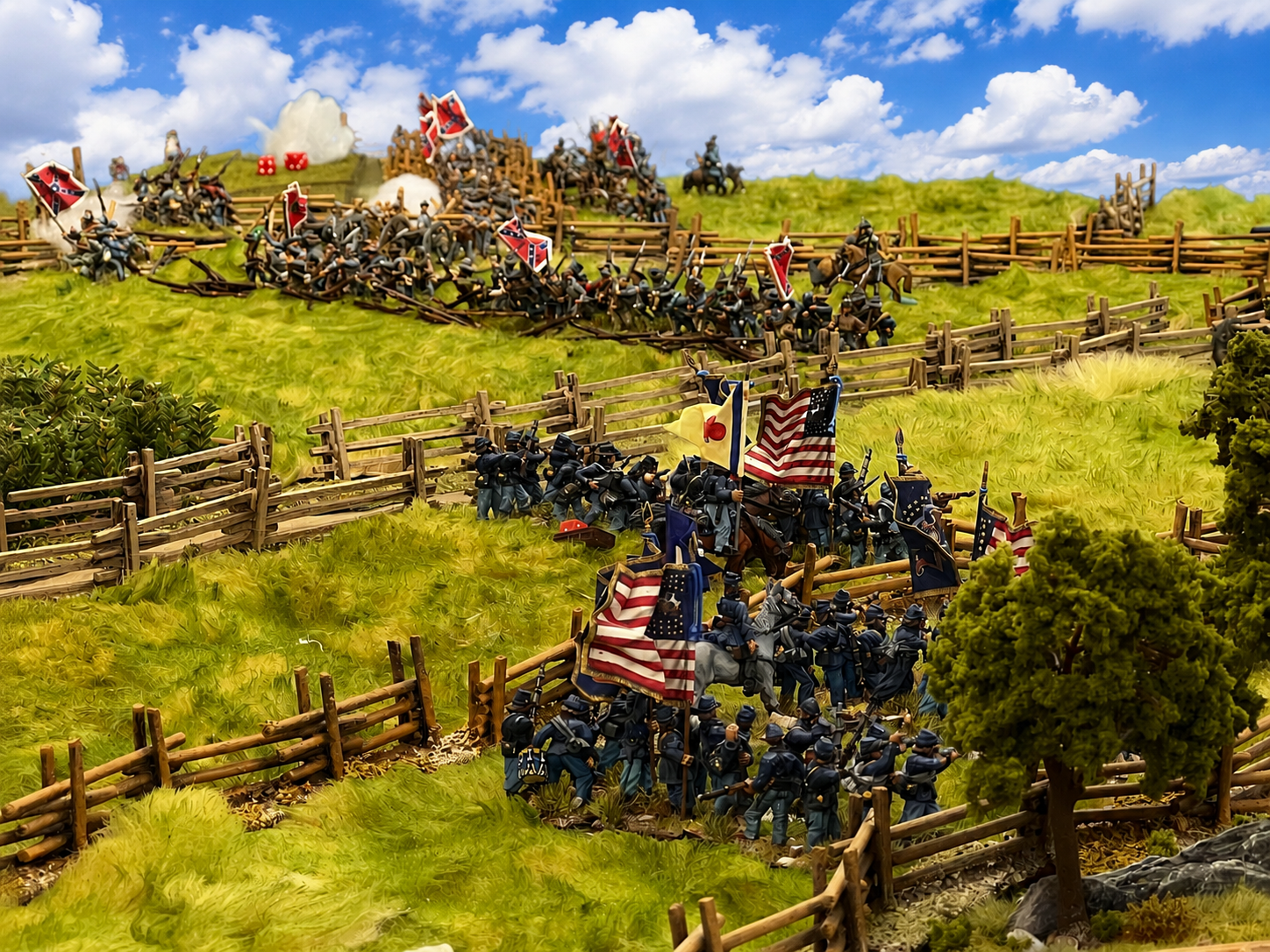 Miniature toy soldiers in a detailed battlefield scene, reenacting a Civil War battle with flags and wooden fences among green grass and trees.