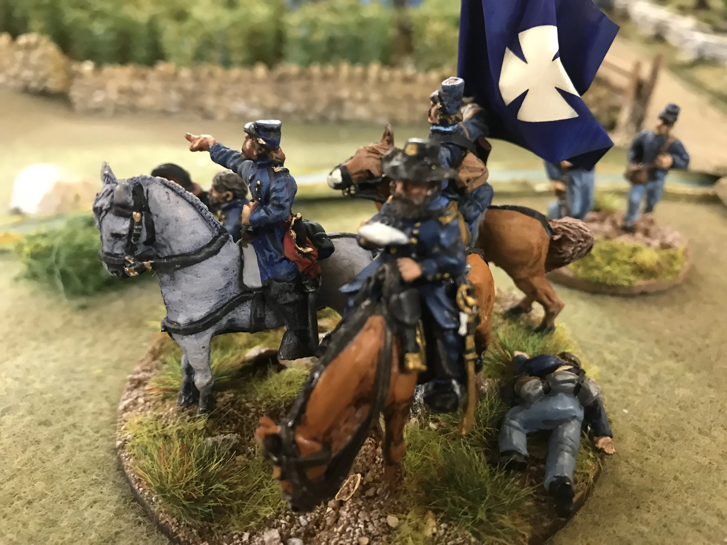 Miniature soldiers on horseback, dressed in blue uniforms, in a forest setting with grass and terrain details.